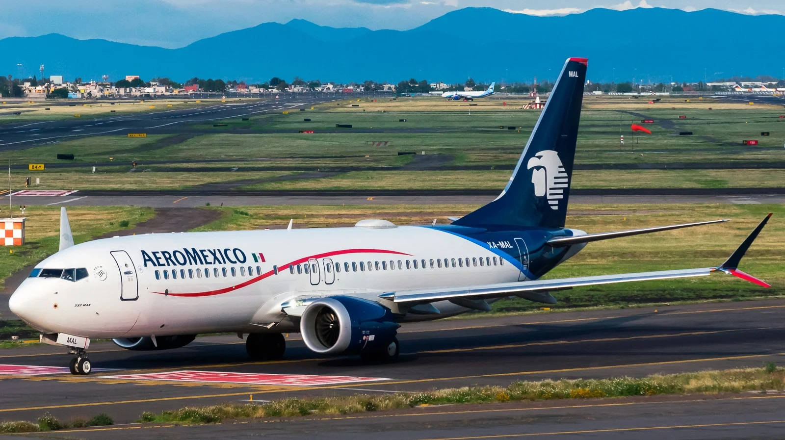 Plane 桌布 壁紙 — 一架 Aeromexico 波音 737 在跑道上滑行，背景有山脈和城鎮，天空局部多雲。