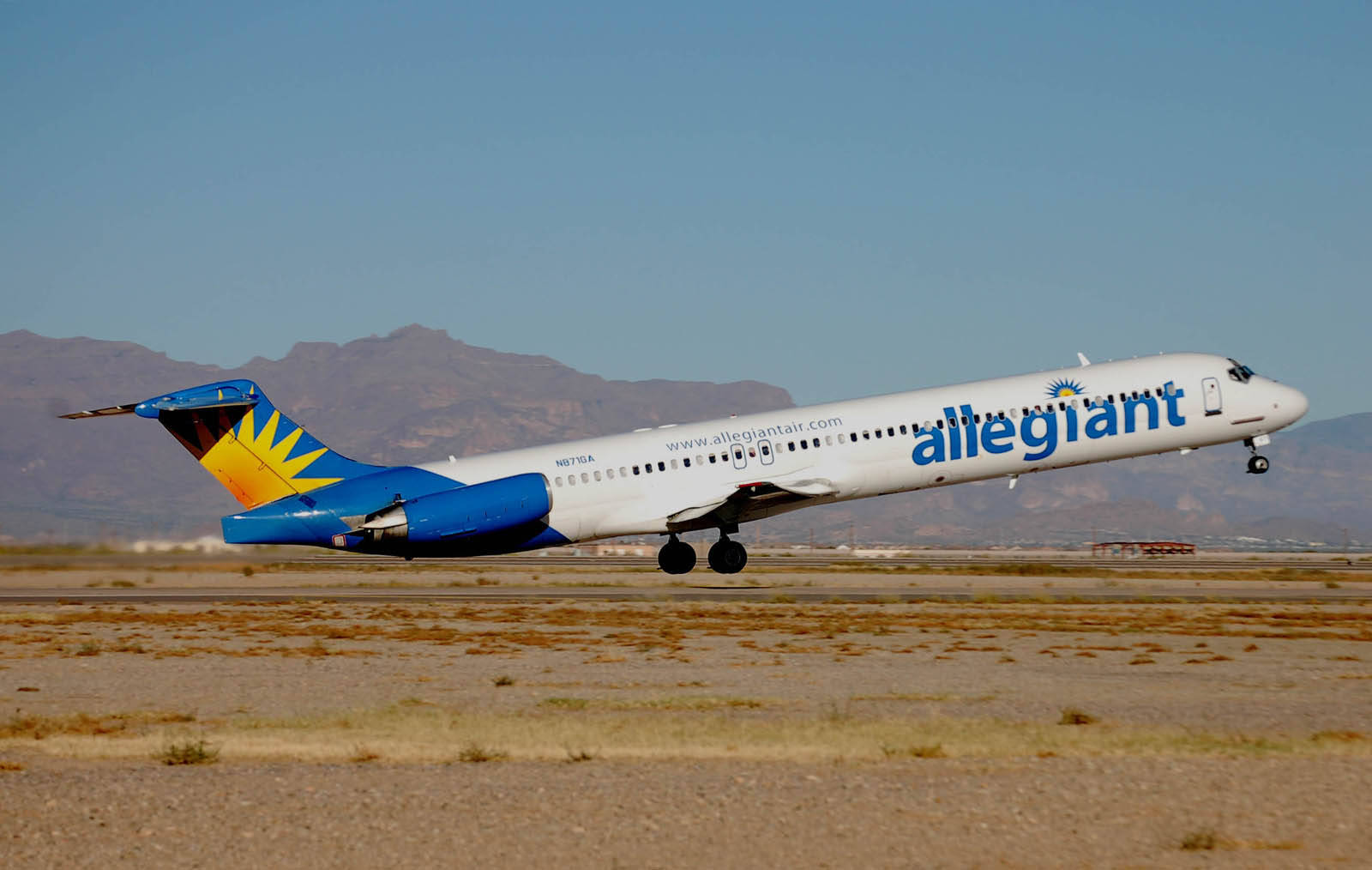 transportation 桌布 壁紙 — 一架 Allegiant Air 噴射機在晴朗藍天下起飛，下方是遠山和乾旱的沙漠地形。