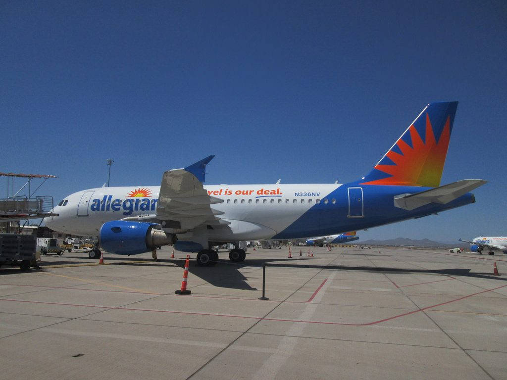 transportation 桌布 壁紙 — 一架 Allegiant Airlines 噴射機停泊在陽光明媚的停機坪上，天空清澈湛藍，遠處有山巒。