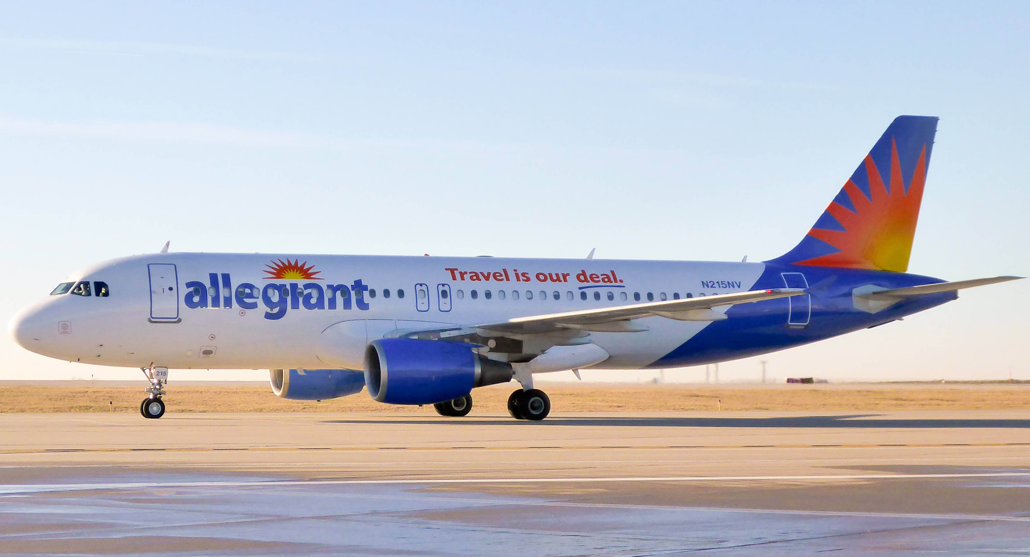 transportation 桌布 壁紙 — 一架 Allegiant Airlines 的噴射機，帶有旭日形尾翼設計，在晴朗的藍天下於跑道上滑行。