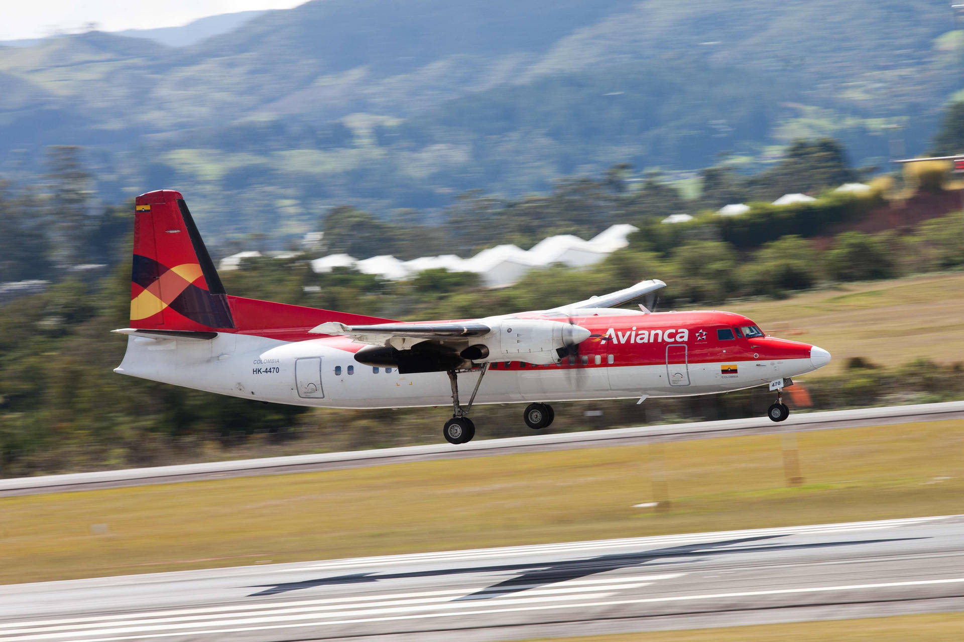 Plane 桌布 壁紙 — 一架 Avianca 區域噴射機從跑道起飛，背景有模糊的綠色山丘和白色建築物。