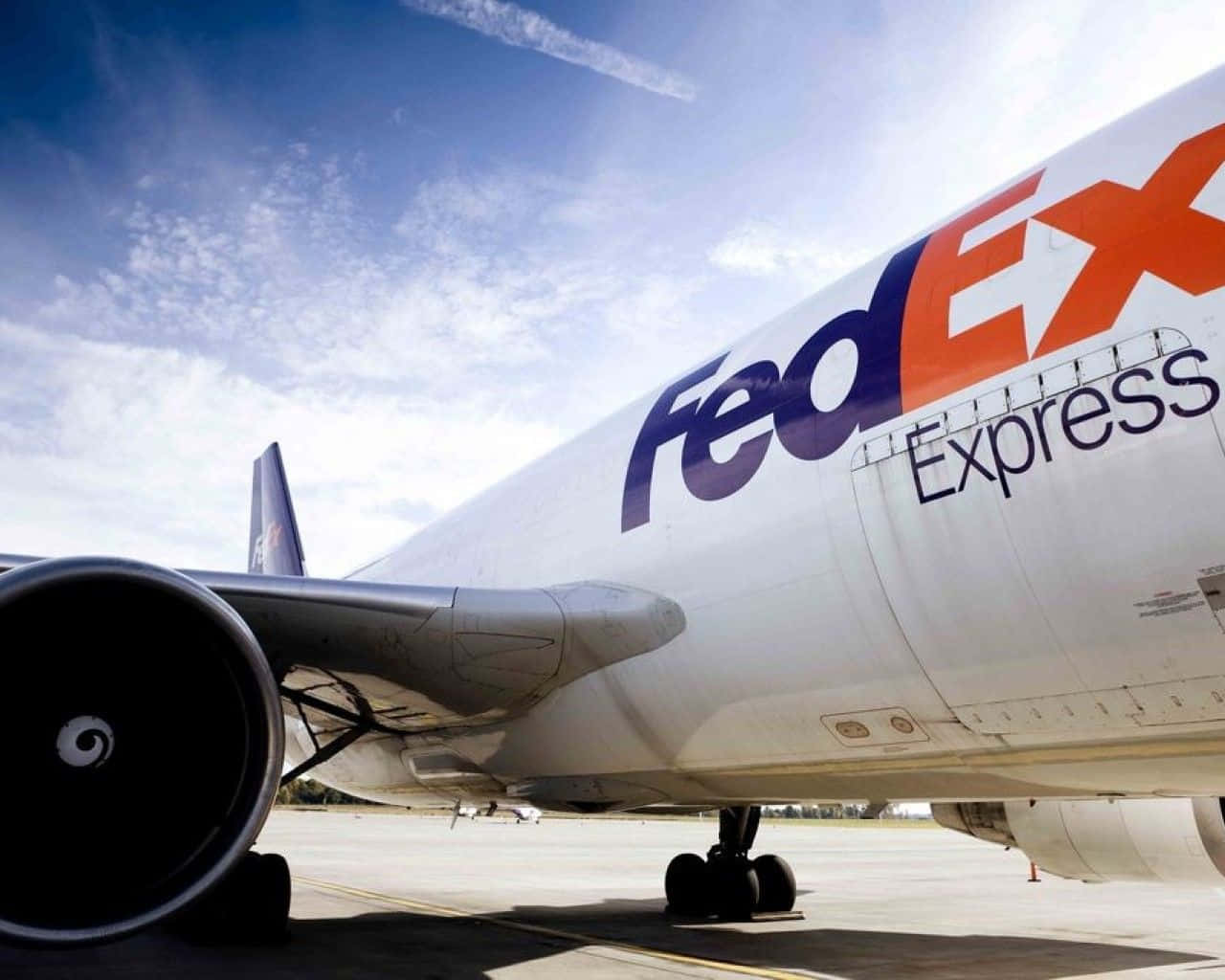 聯邦快遞 桌布 壁紙 — 一架 FedEx Express 貨機停泊在陽光明媚的停機坪上，天空湛藍，白雲點綴。