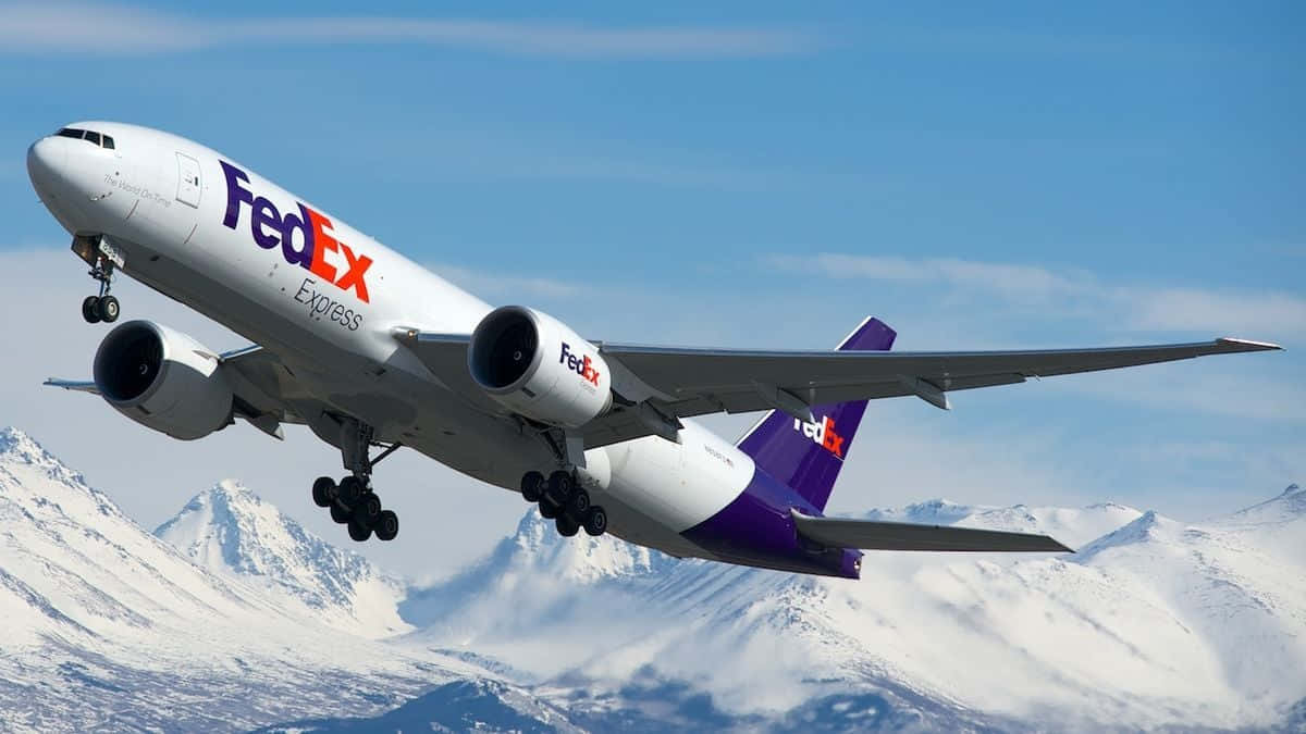 聯邦快遞 桌布 壁紙 — 一架 FedEx Express 貨機在晴朗的藍天下翱翔於白雪覆蓋的山脈之上。
