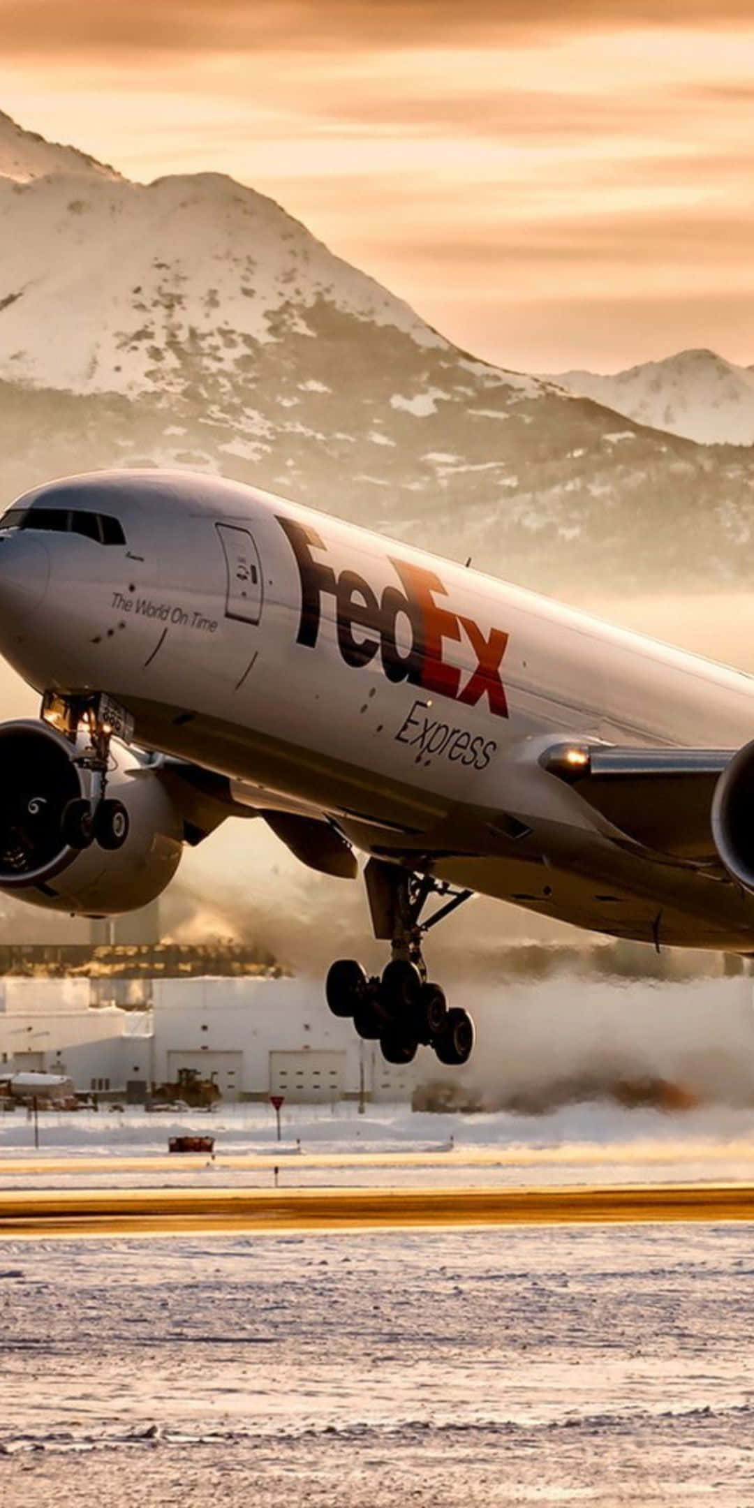 Pixel 3 Plane 桌布 壁紙 — 一架 FedEx Express 貨機從積雪跑道起飛，白雪覆蓋的山峰在金色夕陽下閃耀。