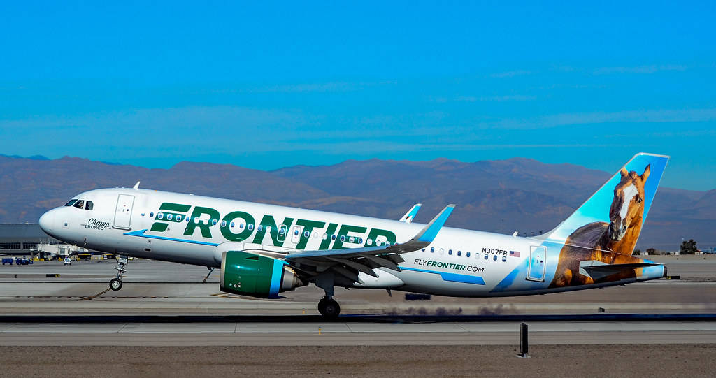 transportation 桌布 壁紙 — 一架 Frontier Airlines 飛機尾部有馬匹圖案，在晴朗藍天和遠山背景下在跑道上滑行。