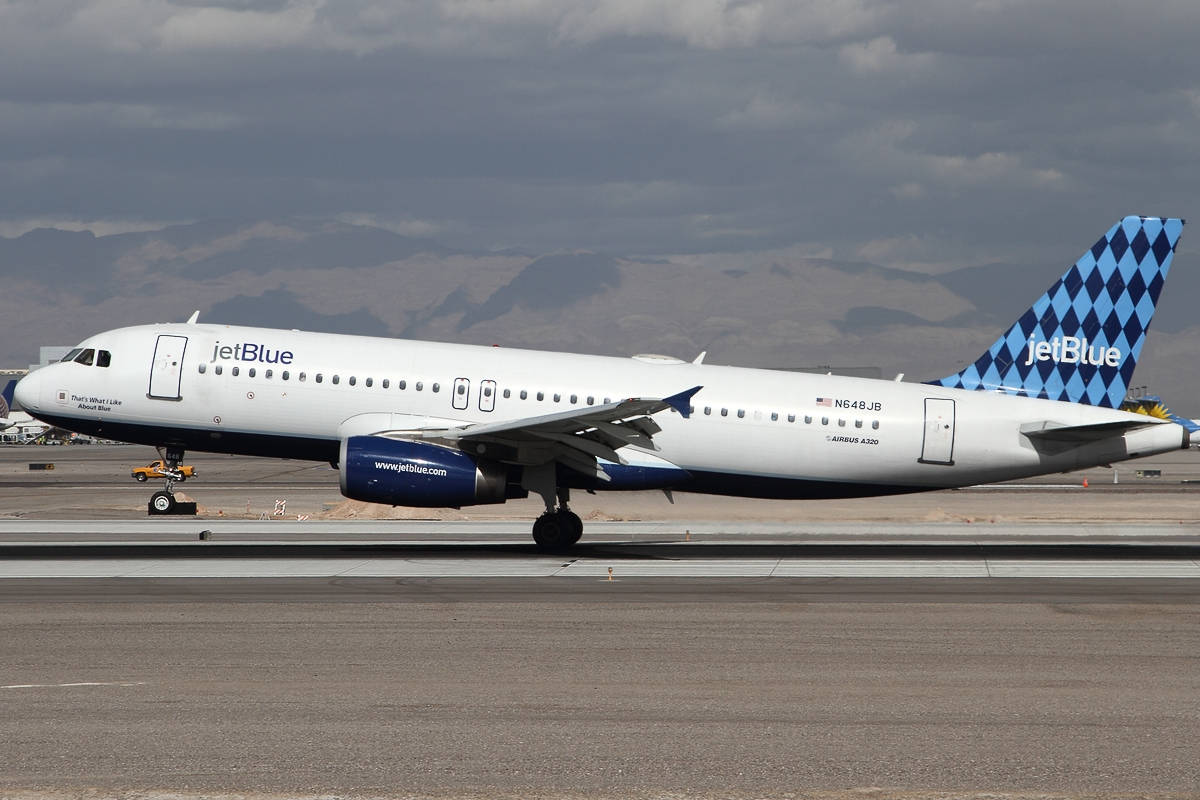 飛機 桌布 壁紙 — 一架 JetBlue 空中巴士 A320 停放在跑道上，背景是山脈，天空多雲。