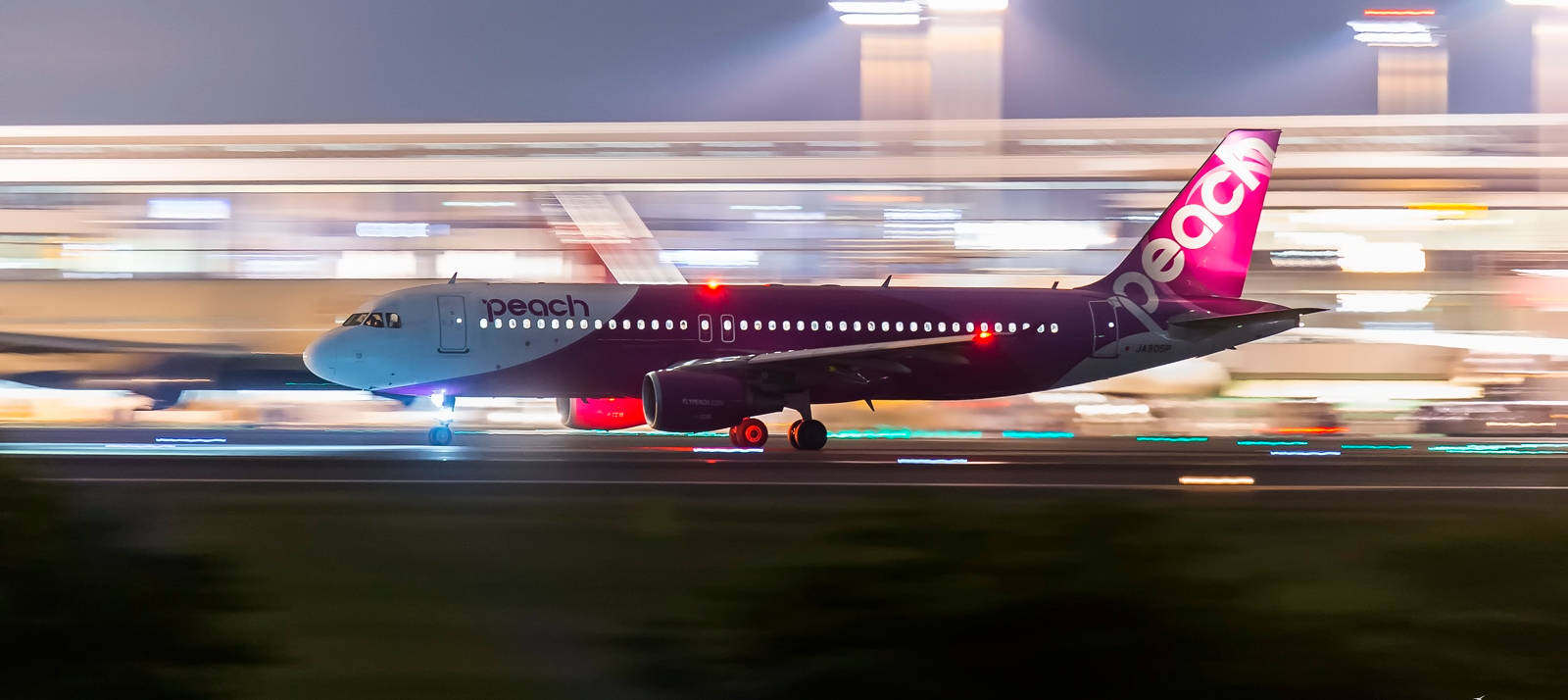Airport 桌布 壁紙 — 一架 Peach Airlines 飛機在夜間高速駛過跑道，機場背景中帶有條紋燈光。