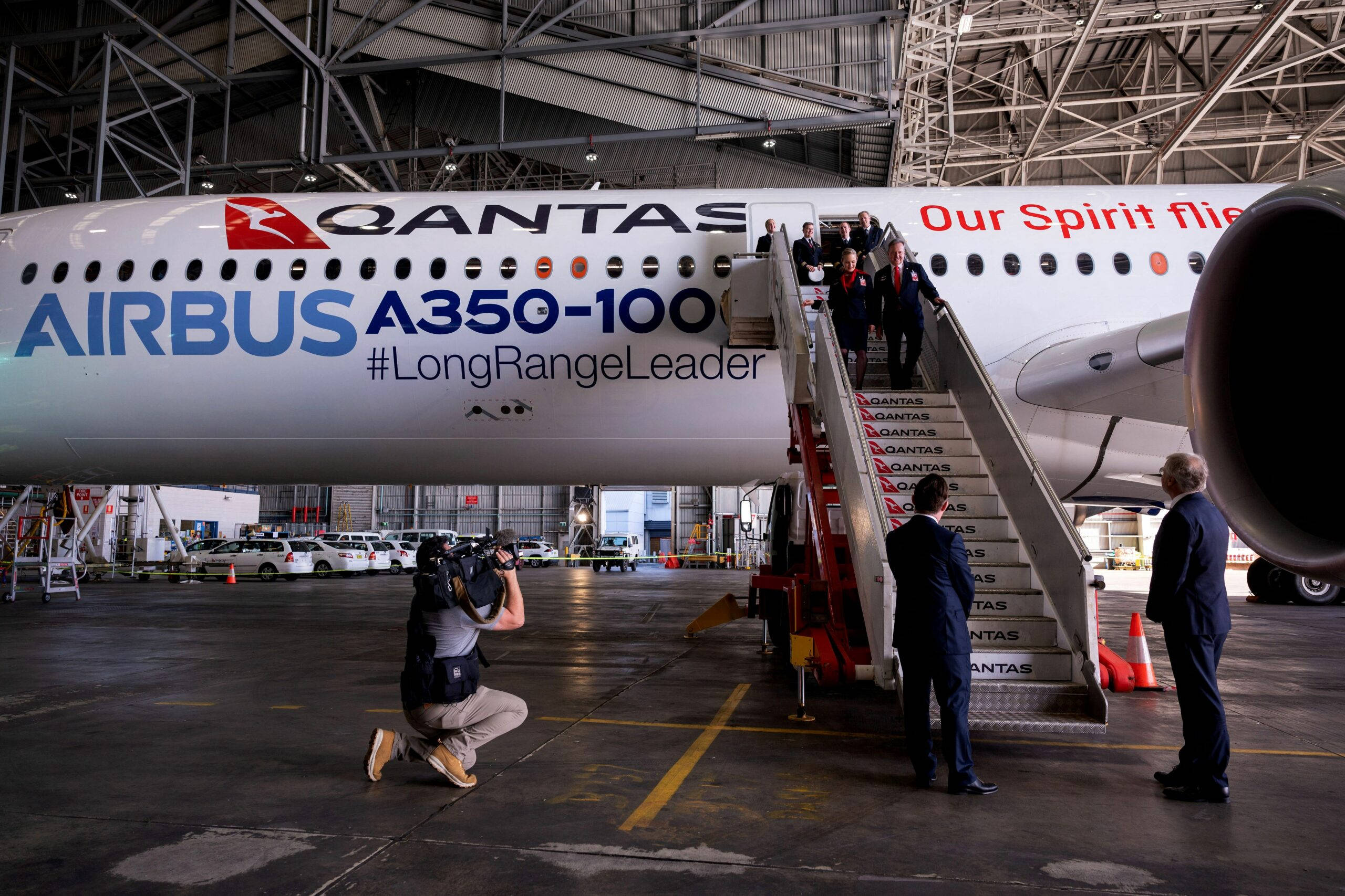 Airport 桌布 壁紙 — 一架 Qantas Airbus A350-100 飛機停放在機庫內，人們正透過樓梯登機，而攝影師正在捕捉這一刻。