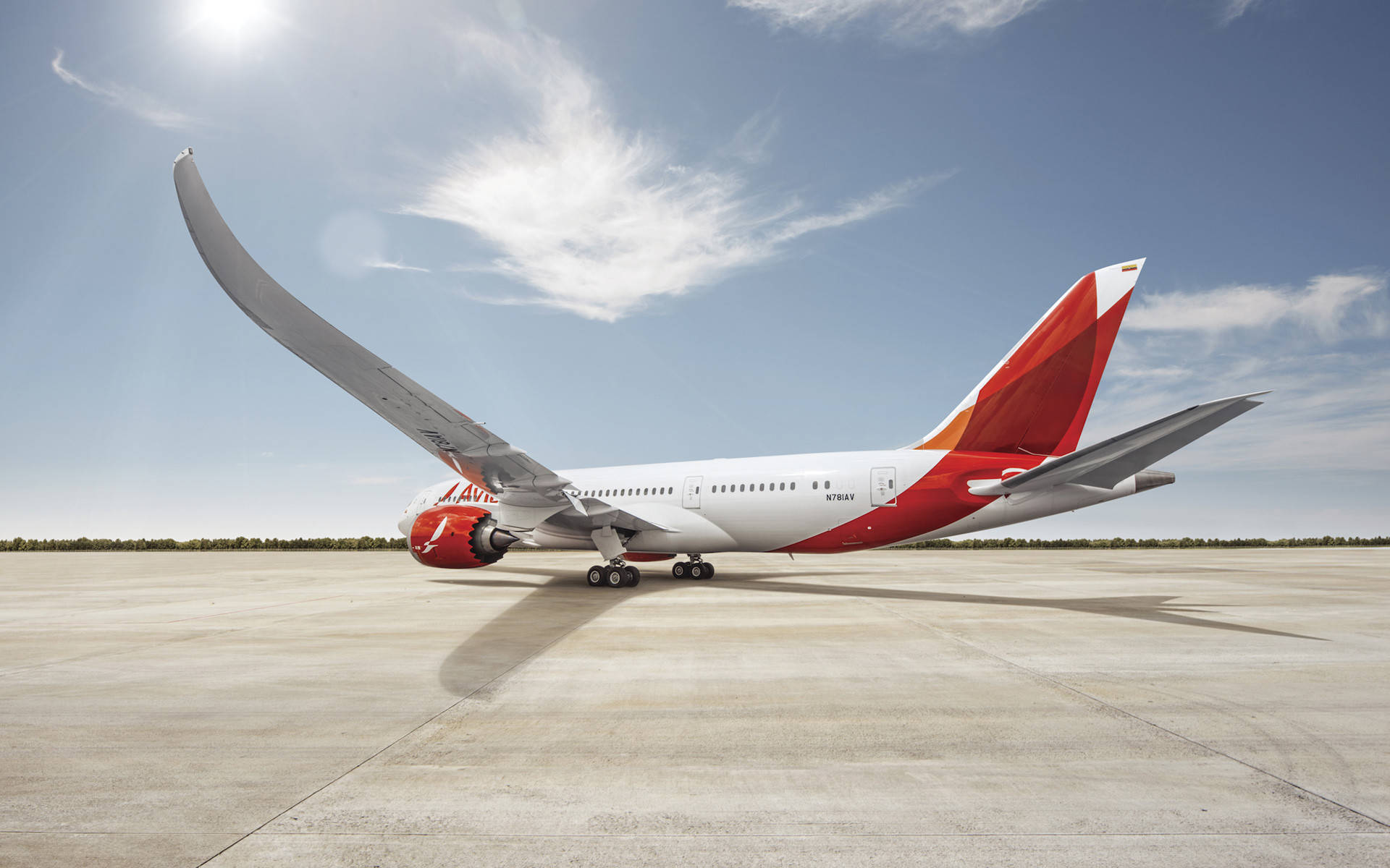  壁紙 — 一架 Qantas 波音 787 夢幻客機，帶有彎曲機翼，停泊在陽光普照的停機坪上，天空湛藍，有薄雲點綴。