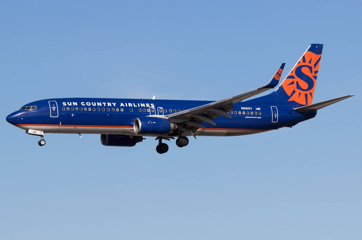 飛機 桌布 壁紙 — 一架 Sun Country Airlines 的波音 737 以藍色和橙色塗裝，在晴朗的藍天下飛行，起落架已放下。