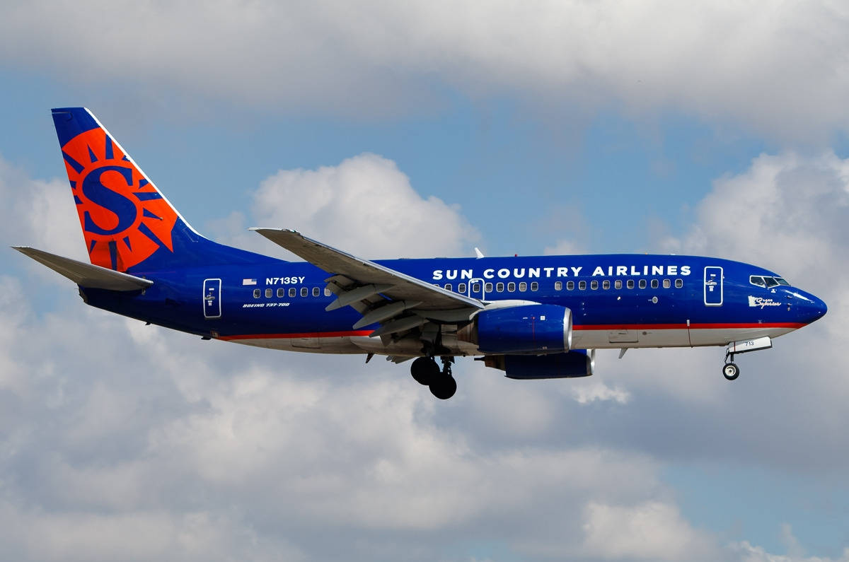 飛機 桌布 壁紙 — 一架 Sun Country Airlines 的波音 737 正在部分多雲的天空中下降，起落架已放下。
