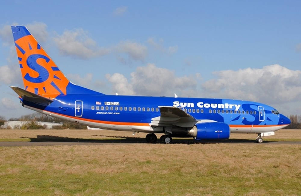 Airport 桌布 壁紙 — 一架 Sun Country Airlines 的波音 737 停放在草地機場上，天空部分多雲，呈現藍色。