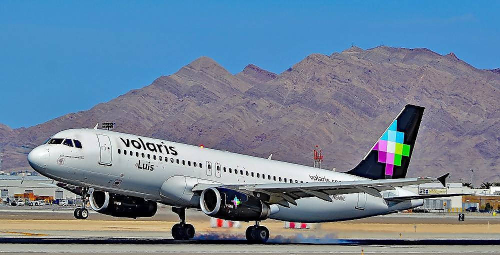 transportation 桌布 壁紙 — 一架 Volaris 飛機在跑道上滑行，崎嶇的棕色山脈在晴朗的藍天下升起。