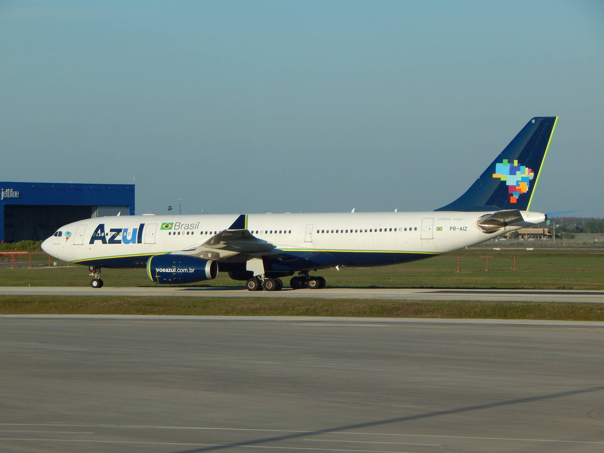  壁紙 — 一架Azul Brasil的空中巴士A330在陽光明媚的機場停機坪上滑行，背景是藍色的飛機庫。
