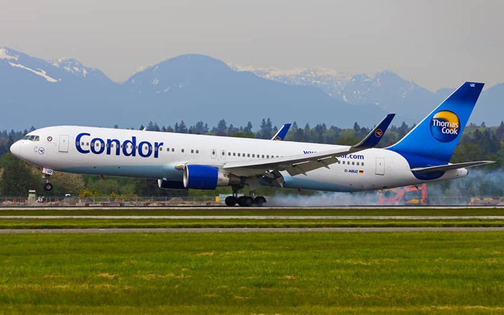 Airport 桌布 壁紙 — 一架Condor Thomas Cook飛機在跑道上滑行，背景是白雪覆蓋的山脈和綠色田野。