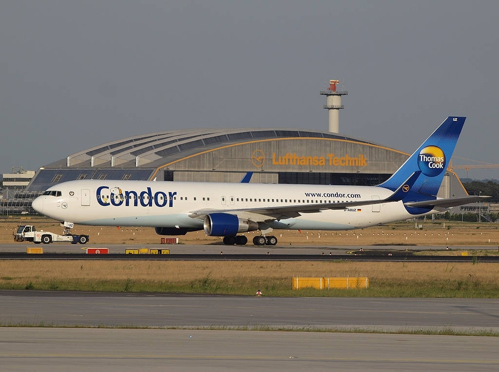 Airport 桌布 壁紙 — 一架Condor Thomas Cook品牌的飛機在機場停機坪上滑行，背景是Lufthansa Technik機庫，天空多雲。