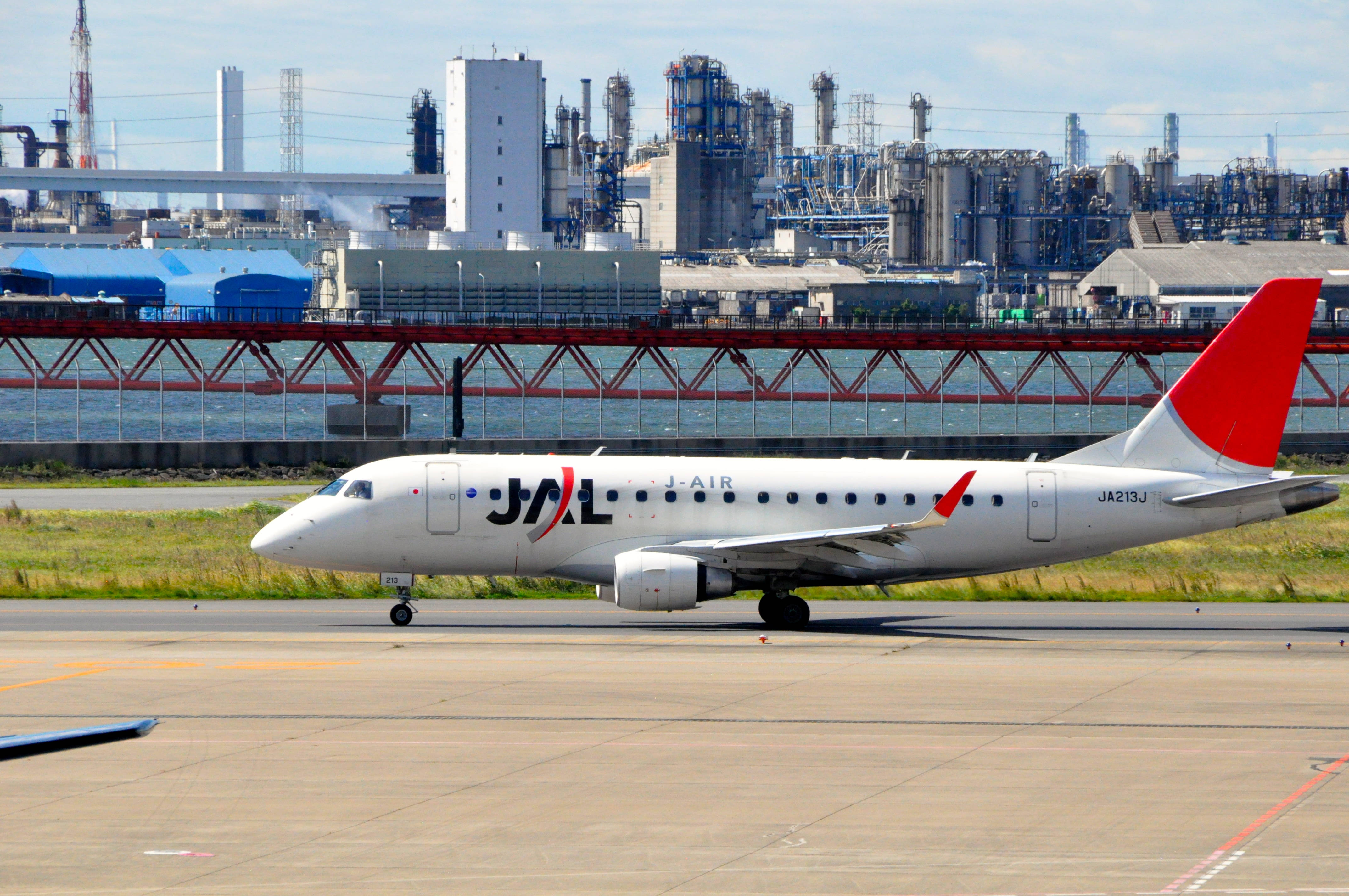 日本 桌布 壁紙 — 一架J-AIR客機在晴朗天空下，以工業綜合體和紅色橋樑為背景，在跑道上滑行。
