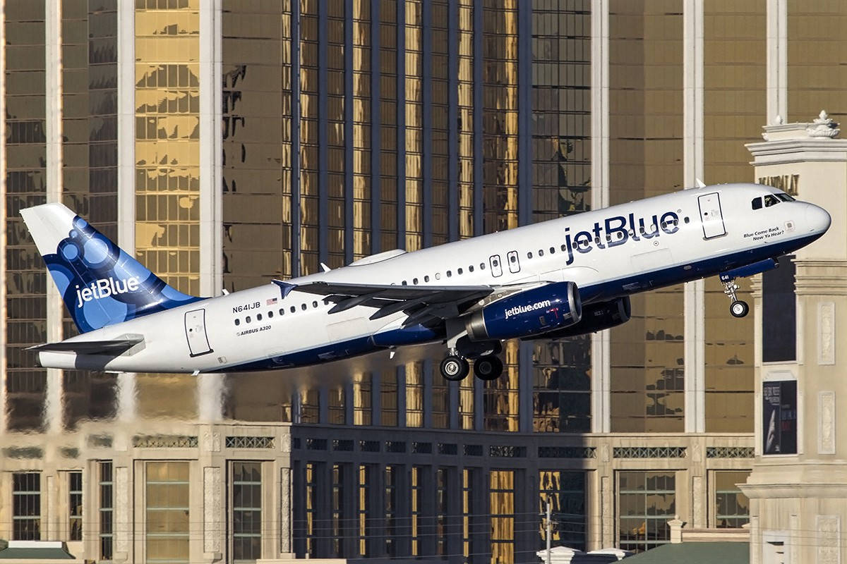 Plane 桌布 壁紙 — 一架JetBlue空中巴士A320在陽光普照、玻璃摩天大樓反射金色光芒的城市景觀上空低飛降落。
