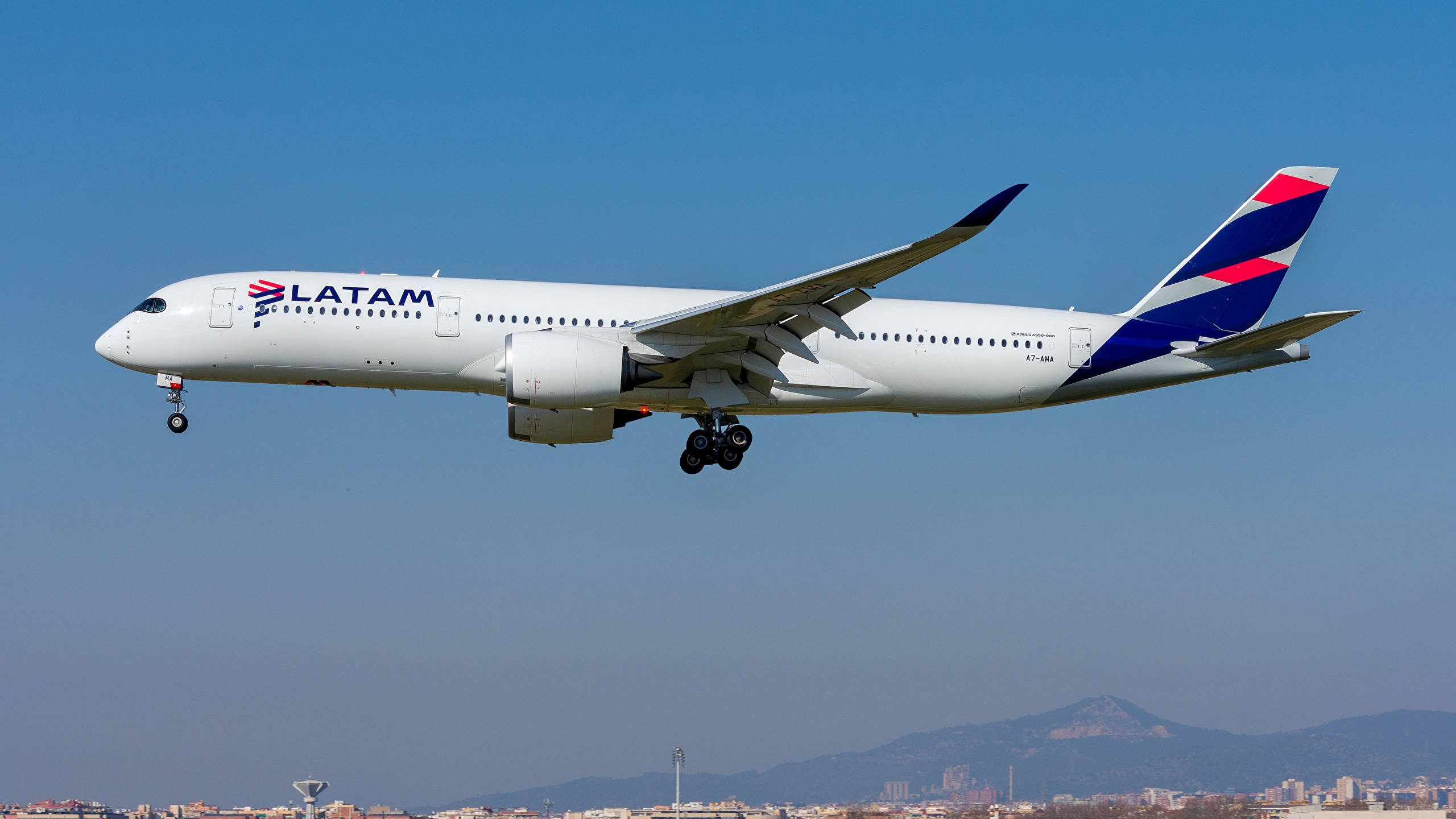 flying 桌布 壁紙 — 一架LATAM航空的空中巴士A350在晴朗藍天下優雅下降，下方是遠山和城市景觀。