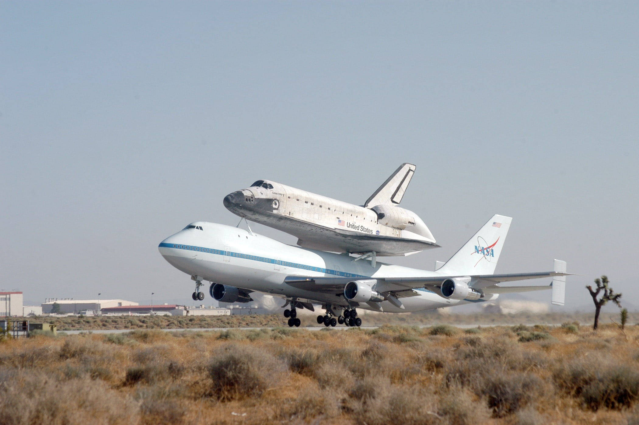 飛機 桌布 壁紙 — 一架NASA太空梭安裝在改裝的波音747上，在朦朧的天空下從沙漠跑道起飛。
