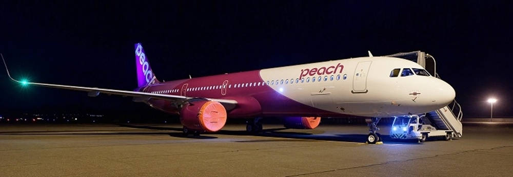 Airport 桌布 壁紙 — 一架Peach Airlines飛機在夜間停機坪上被照亮，帶有充滿活力的紫色和粉紅色調，在人造燈光下閃耀。