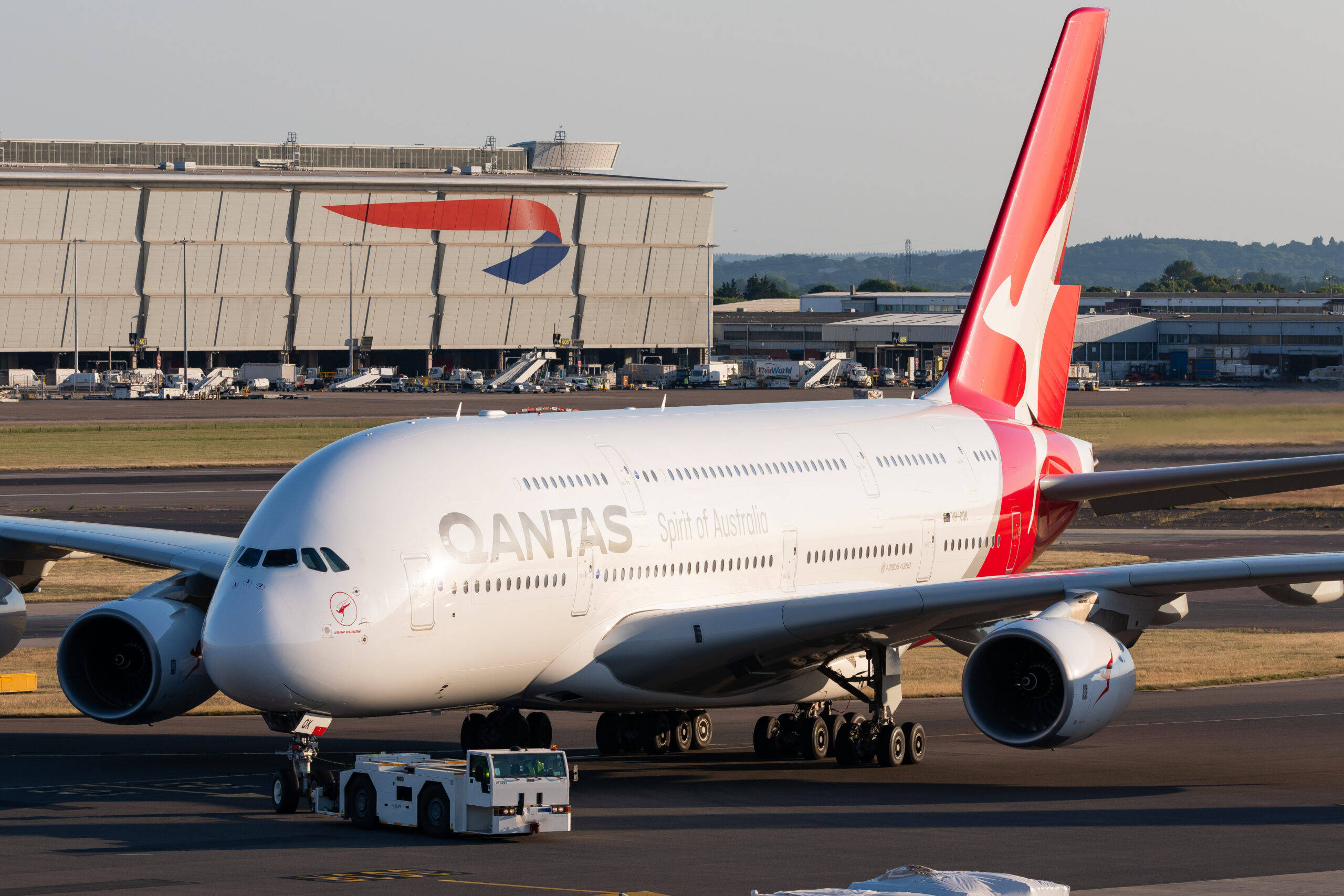 Airport 桌布 壁紙 — 一架Qantas Airbus A380 'Spirit of Australia'正在機場停機坪被拖行，背景有機庫和遠處的山丘。