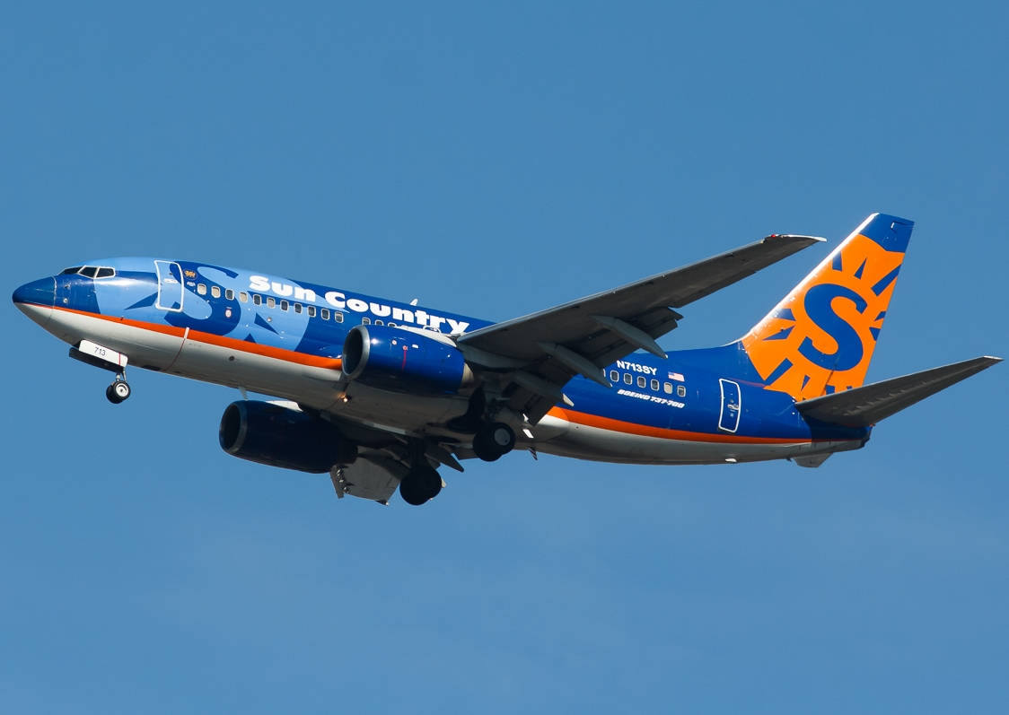 飛機 桌布 壁紙 — 一架Sun Country Airlines的波音737，藍橙塗裝，起落架放下，在晴朗藍天中翱翔。