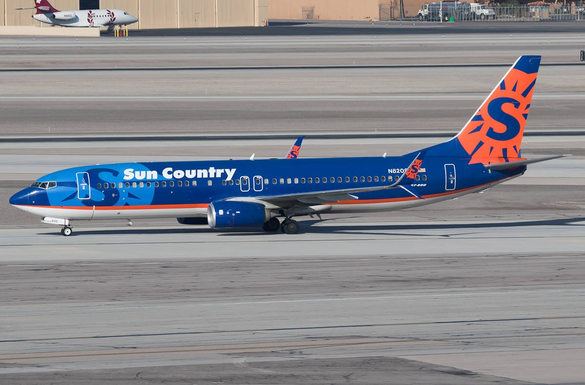 Airport 桌布 壁紙 — 一架Sun Country Airlines波音737，帶有藍色和橙色塗裝，在陽光明媚的機場停機坪上滑行。