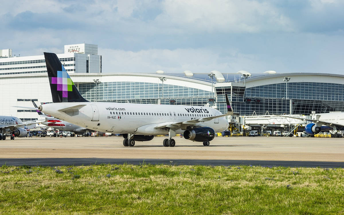 transportation 桌布 壁紙 — 一架Volaris飛機在陽光明媚的機場停機坪上滑行，背景是現代化的航站樓和多雲的天空。