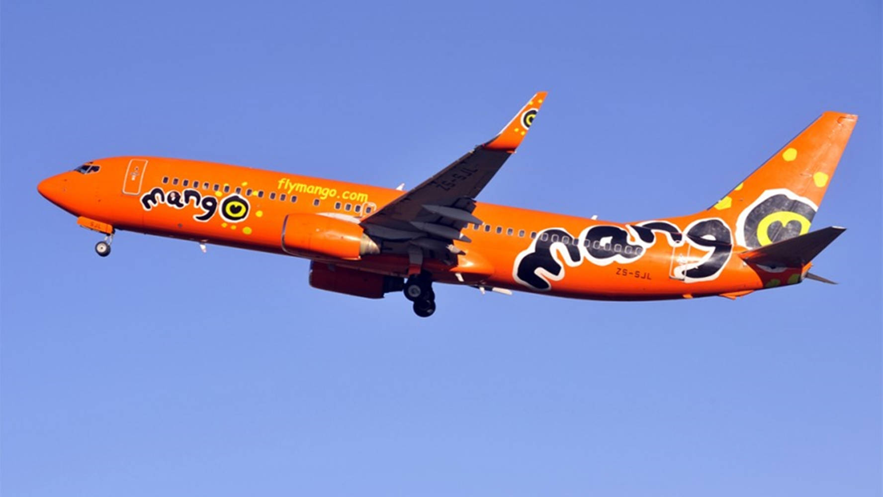 飛機 桌布 壁紙 — 一架亮橙色的Mango Airlines飛機帶著粗體黑色標誌在晴朗藍天中翱翔，進行日間飛行。