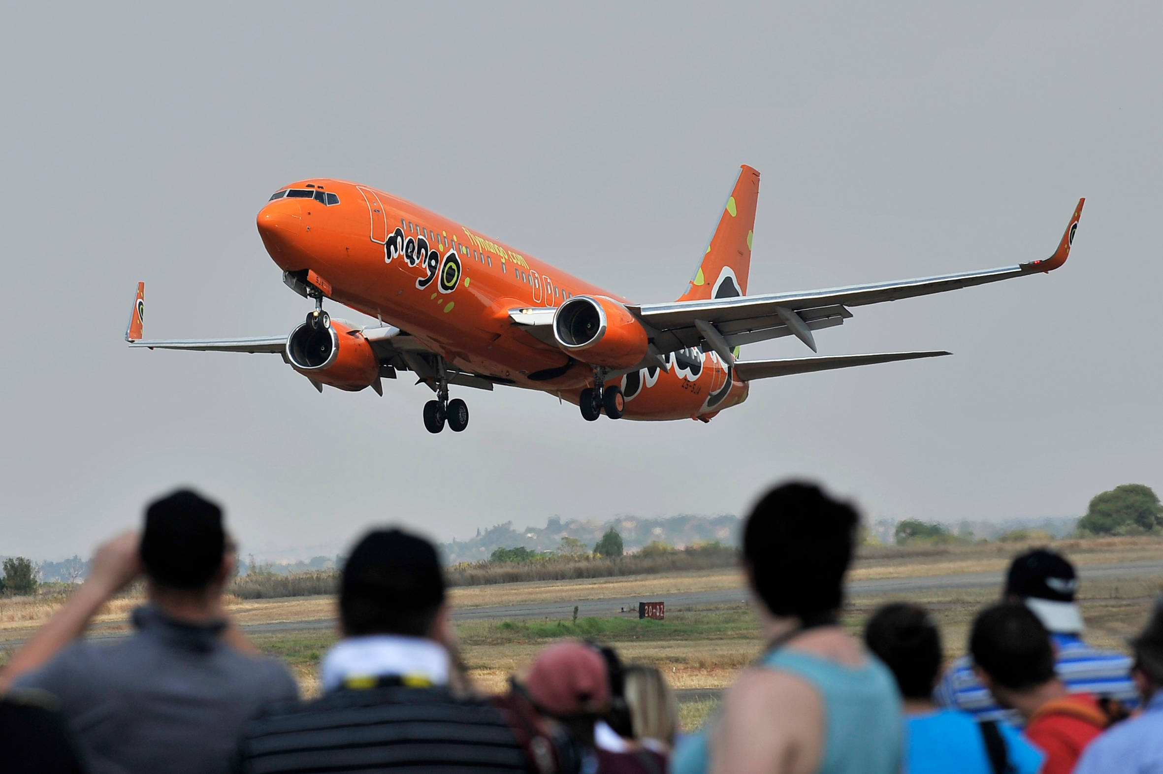 飛機 桌布 壁紙 — 一架亮橙色的Mango Airlines飛機從跑道起飛，觀眾從下方觀看。