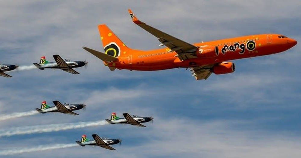 飛機 桌布 壁紙 — 一架亮橙色的Mango Airlines噴射機在雲層密佈的天空上飛過復古螺旋槳飛機，留下白色煙跡。
