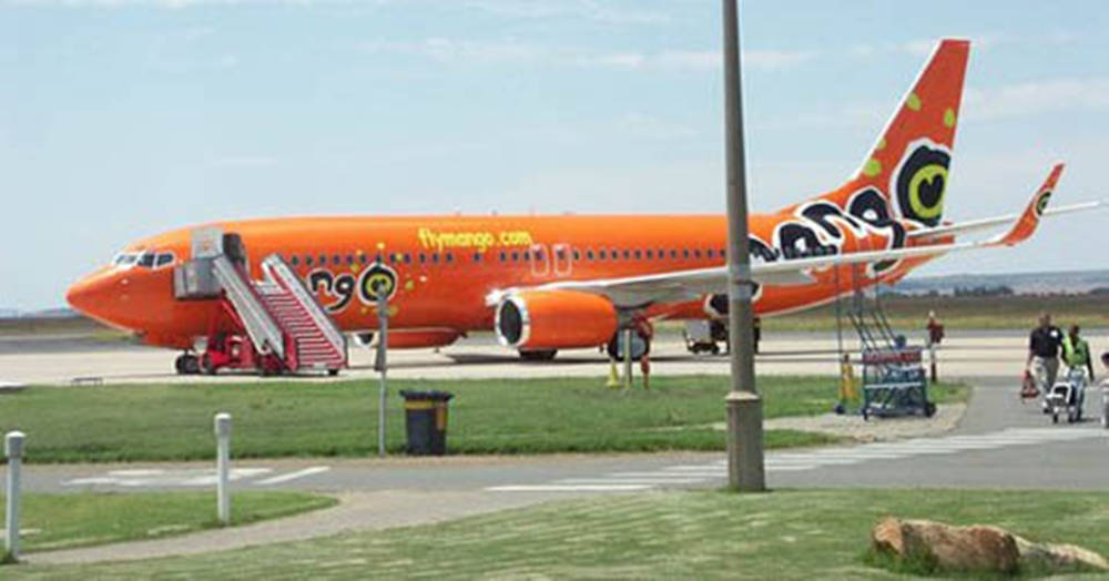 Grass 桌布 壁紙 — 一架亮橙色的Mango Airlines飛機停在機場停機坪上，乘客在晴朗的藍天下通過樓梯登機。