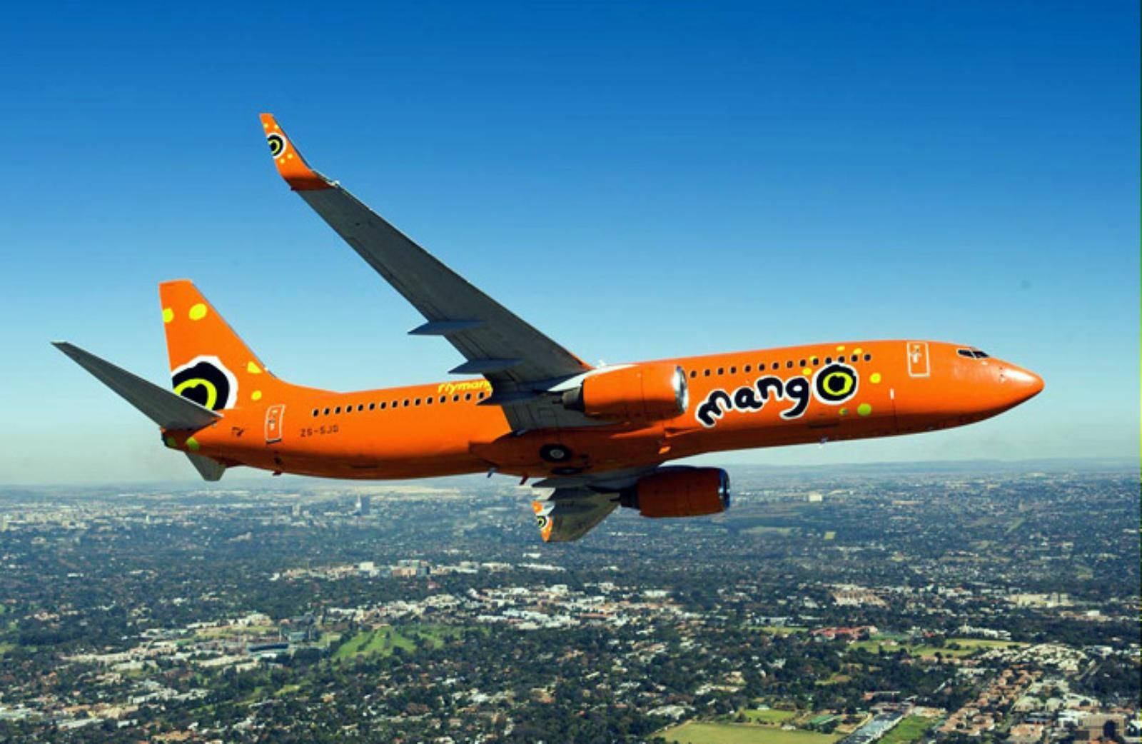 飛機 桌布 壁紙 — 一架亮橙色的Mango Airlines噴射機在晴朗藍天下翱翔於廣闊的郊區景觀之上。