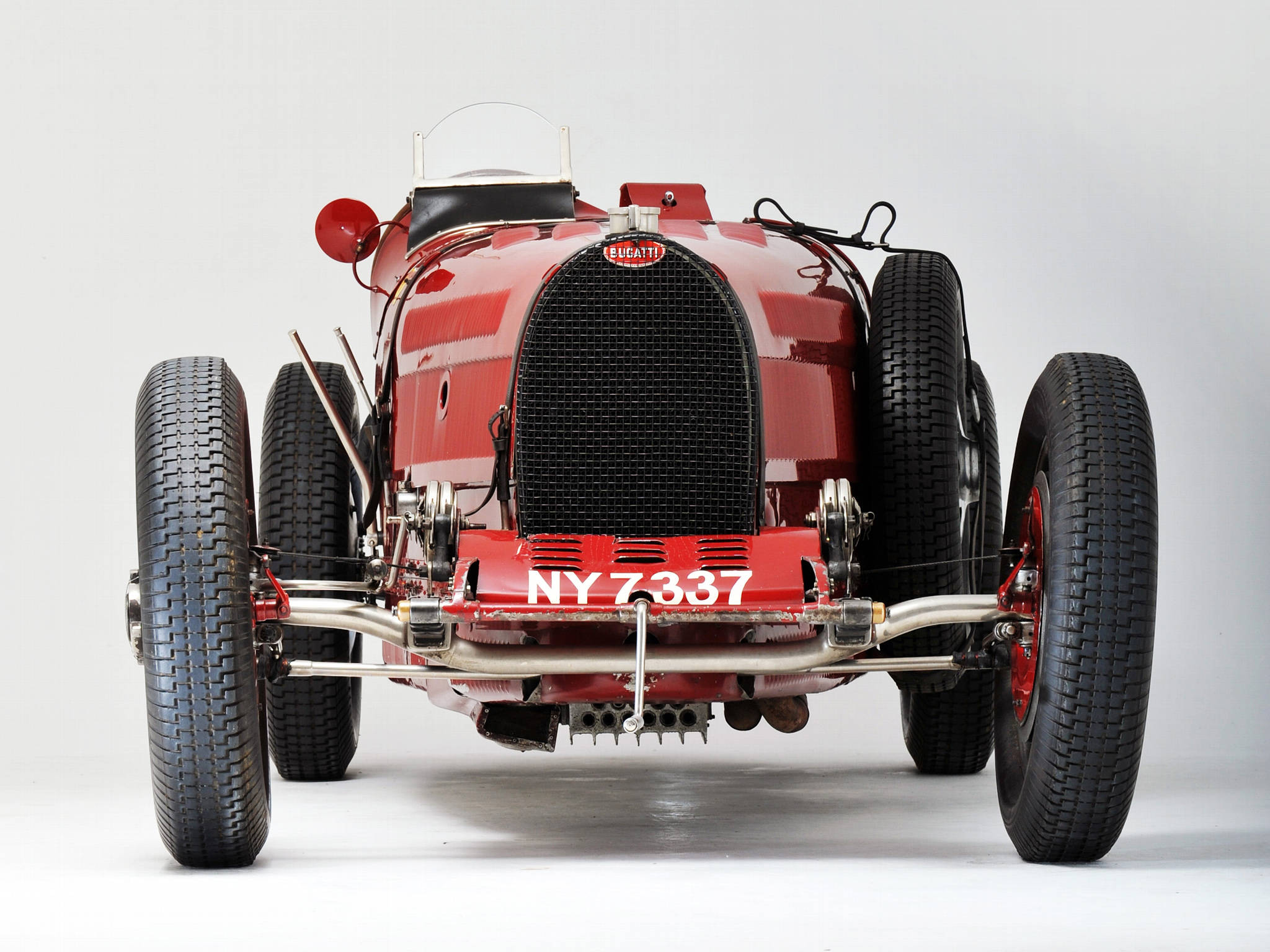bugatti iPhone 桌布 壁紙 — 一架亮面紅色復古Bugatti賽車，帶有外露機械結構和NY7337車牌，在純白色背景前拍攝。