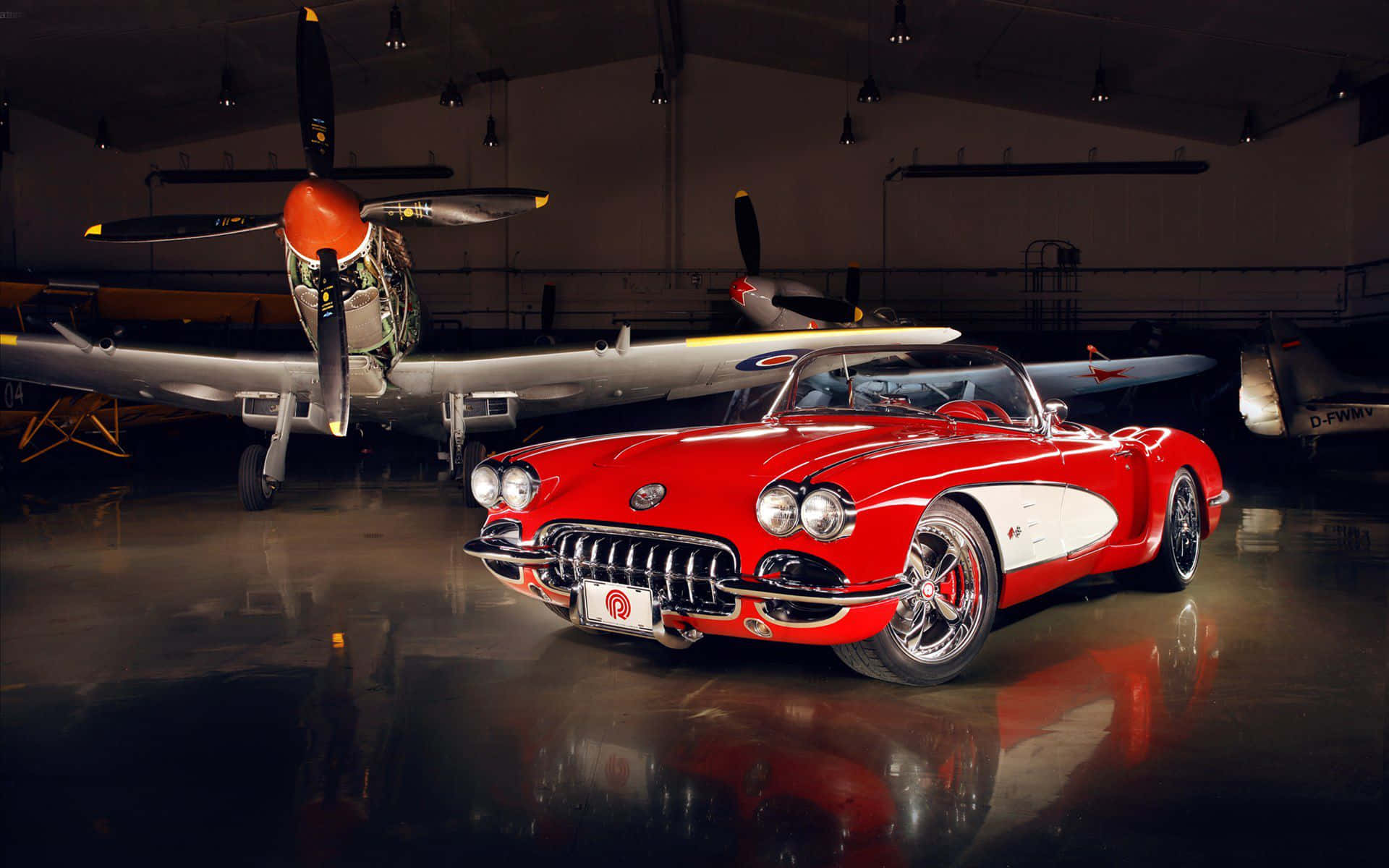 classic 桌布 壁紙 — 一架亮麗的紅色經典Corvette敞篷車在昏暗的機庫中，於聚光燈下與復古螺旋槳飛機並列閃耀。