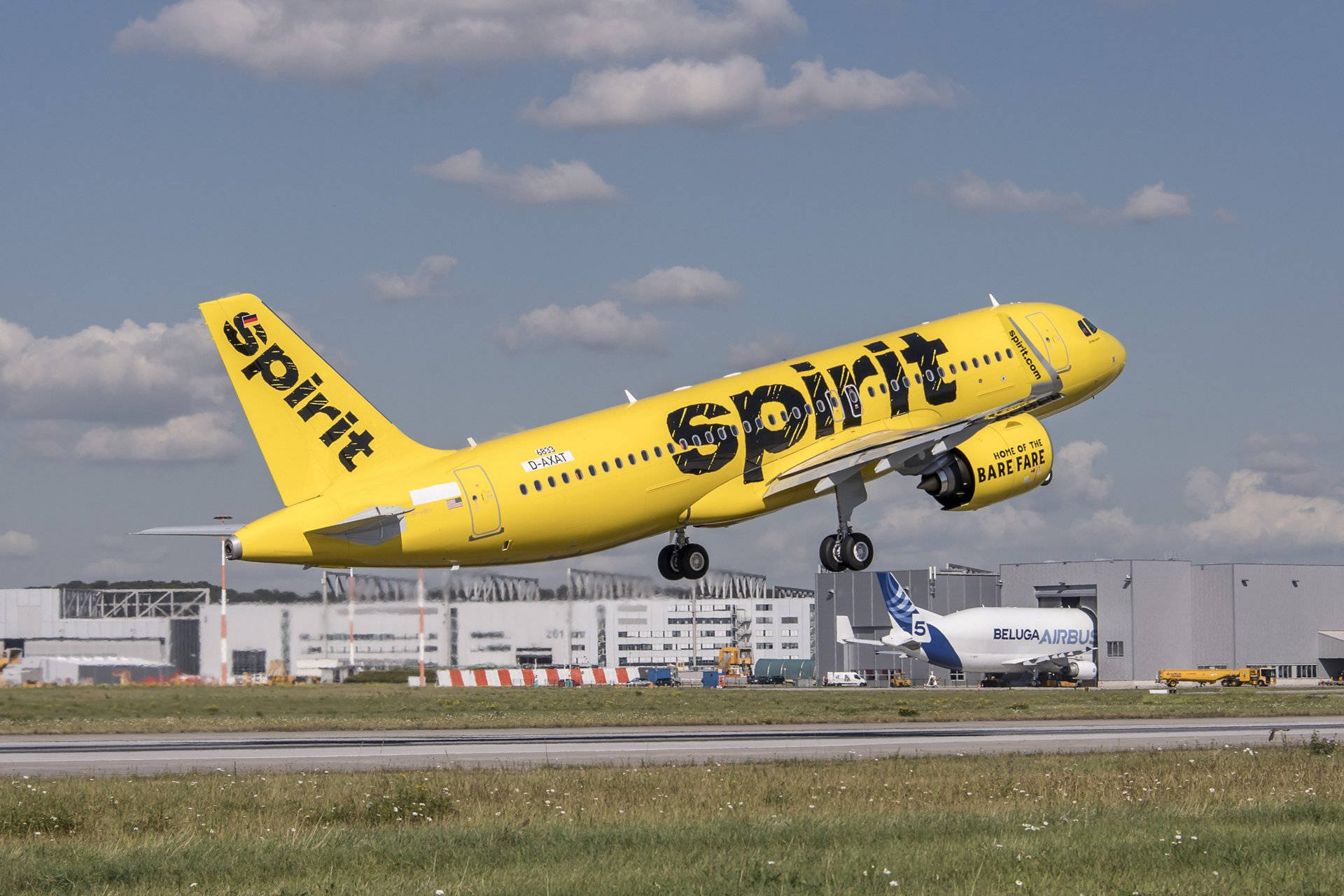 飛機 桌布 壁紙 — 一架亮黃色的Spirit Airlines空中巴士A320在部分多雲的藍天和背景的機場建築物襯托下起飛。