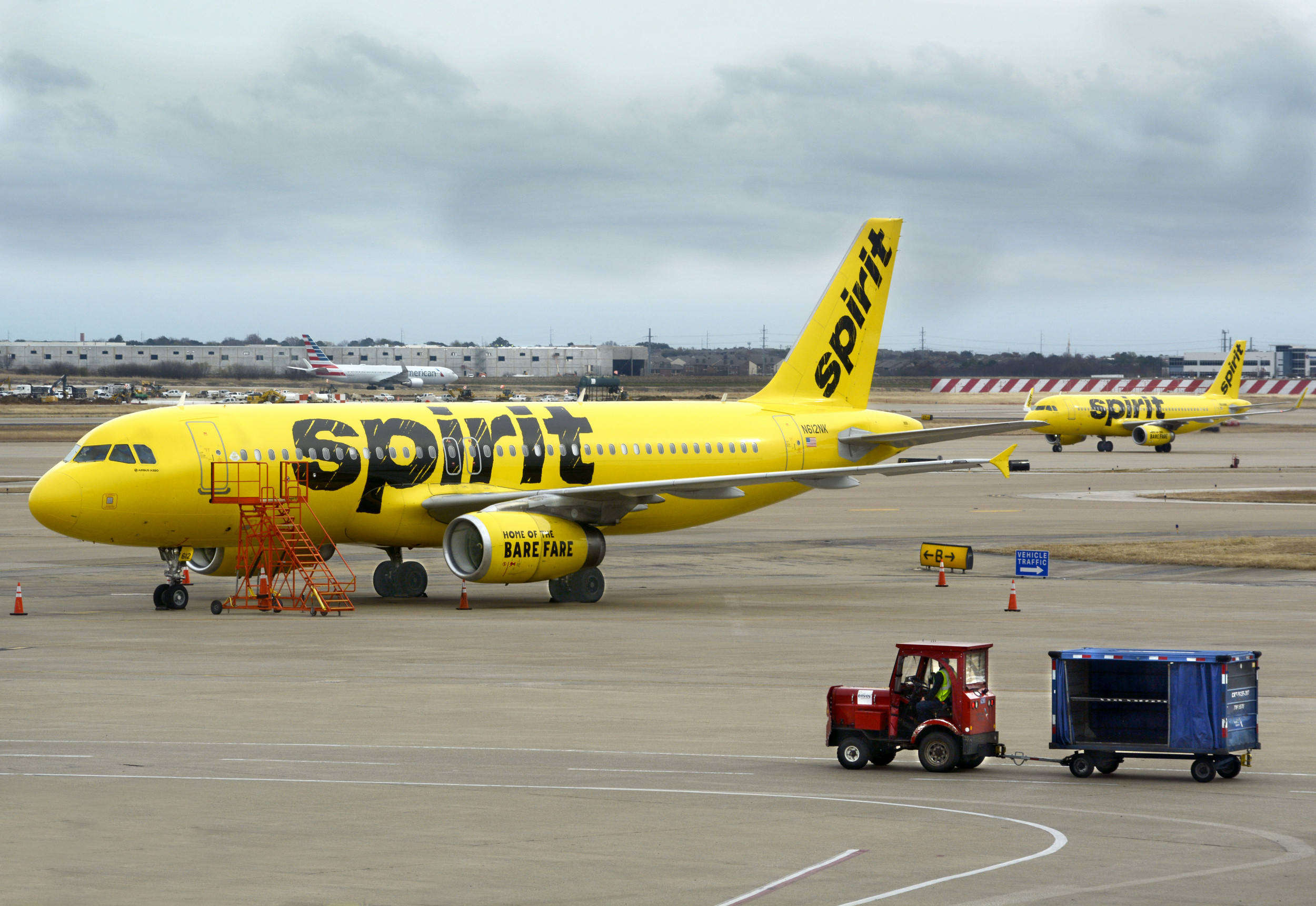 飛機 桌布 壁紙 — 一架亮黃色的Spirit Airlines噴射機停在機場停機坪上，天空多雲，附近有地勤人員和設備。