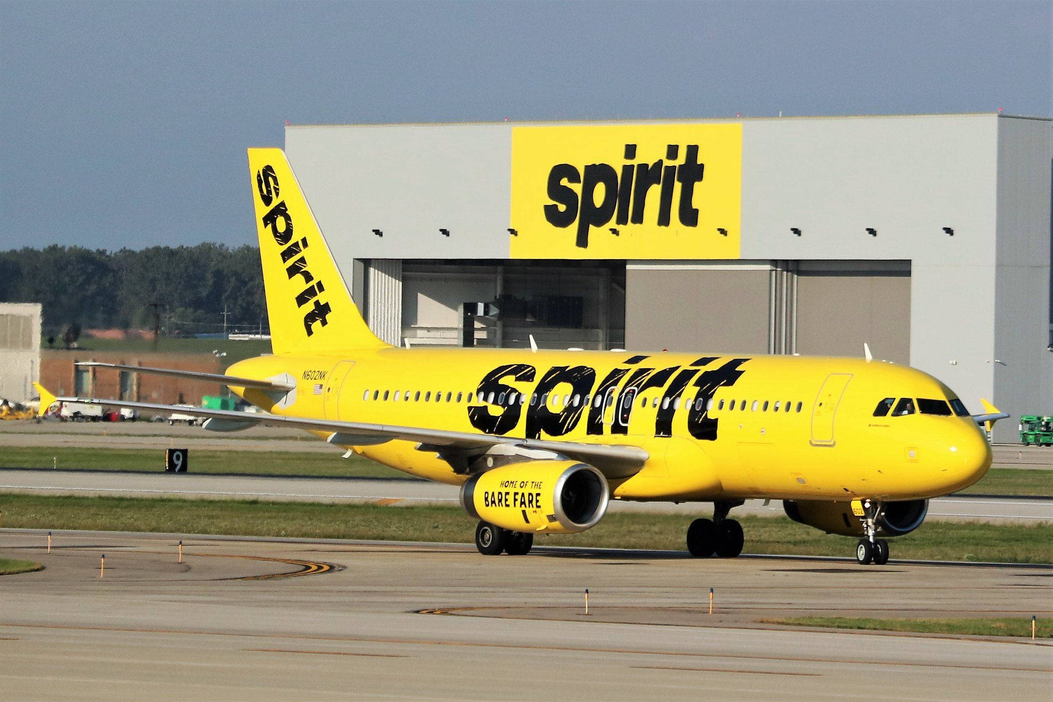 飛機 桌布 壁紙 — 一架亮黃色的Spirit Airlines飛機在機場停機坪滑行，背景是相同品牌的機庫。