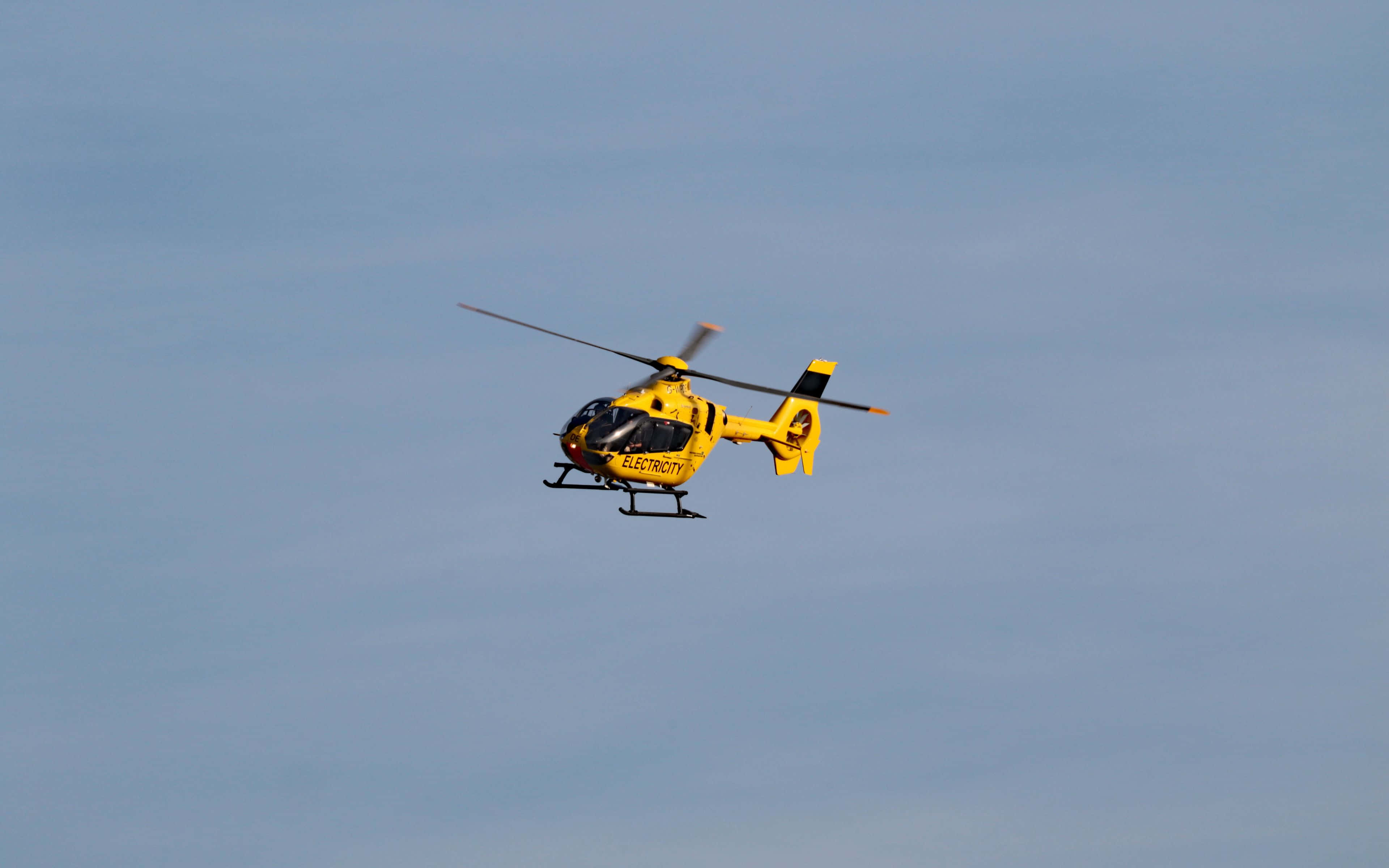4K Helicopters 桌布 壁紙 — 一架亮黃色的多用途直升機在晴朗的藍天中翱翔，旋翼轉動。
