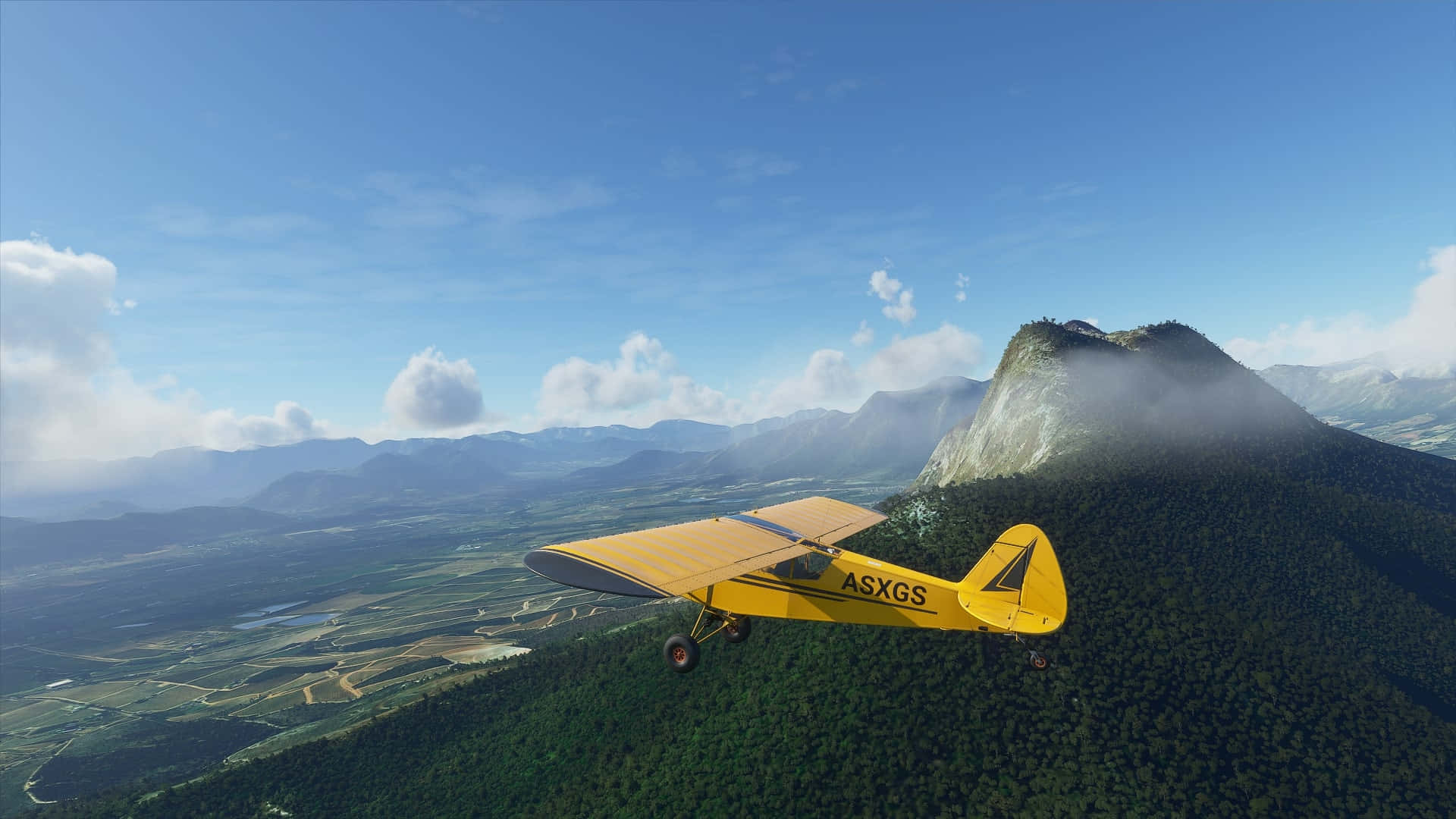 1080p Microsoft Flight Simulator 桌布 壁紙 — 一架亮黃色的復古飛機在晴朗藍天和零星白雲下，翱翔於鬱鬱蔥蔥的綠色山脈之上。
