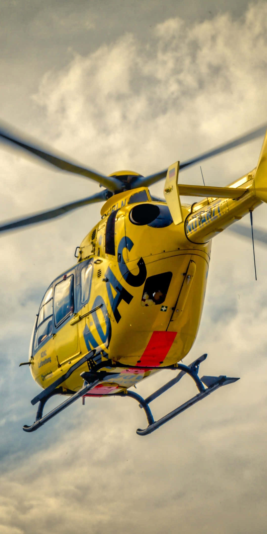 Helicopter 桌布 壁紙 — 一架亮黃色的救援直升機在雲層密佈的天空中盤旋，旋翼轉動。