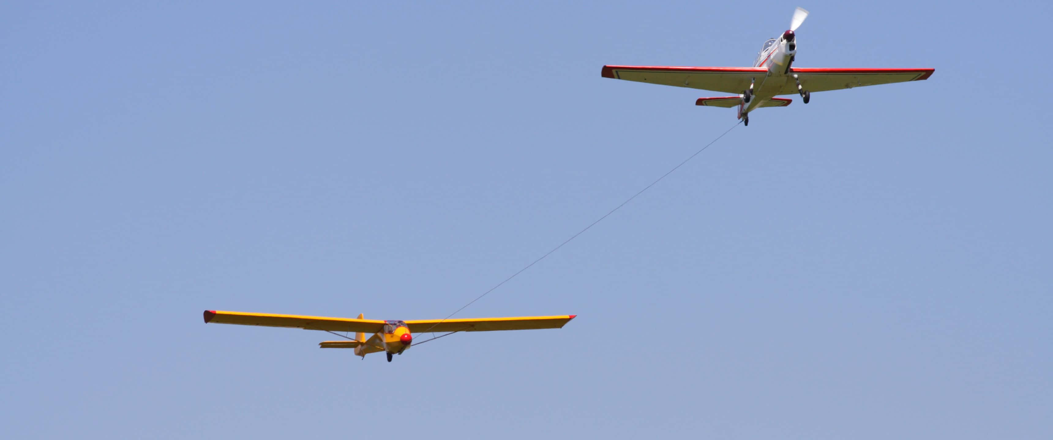3440x1440p Small Planes 桌布 壁紙 — 一架亮黃色的滑翔機被一架紅白相間的飛機拖曳，背景是清澈的藍天。