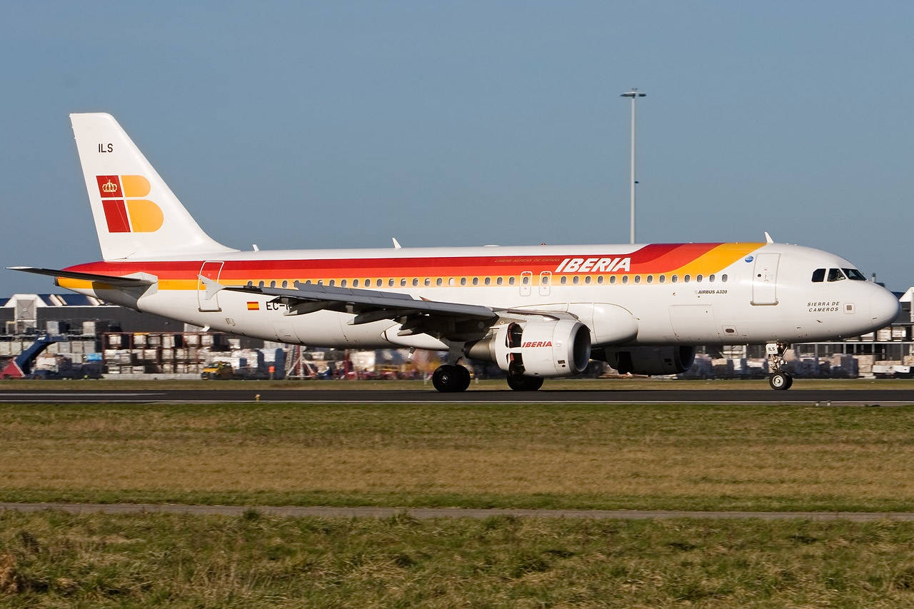 Grass 桌布 壁紙 — 一架伊比利亞航空的空中巴士A320在晴朗藍天下，以機場建築物和貨運集裝箱為背景，在跑道上滑行。