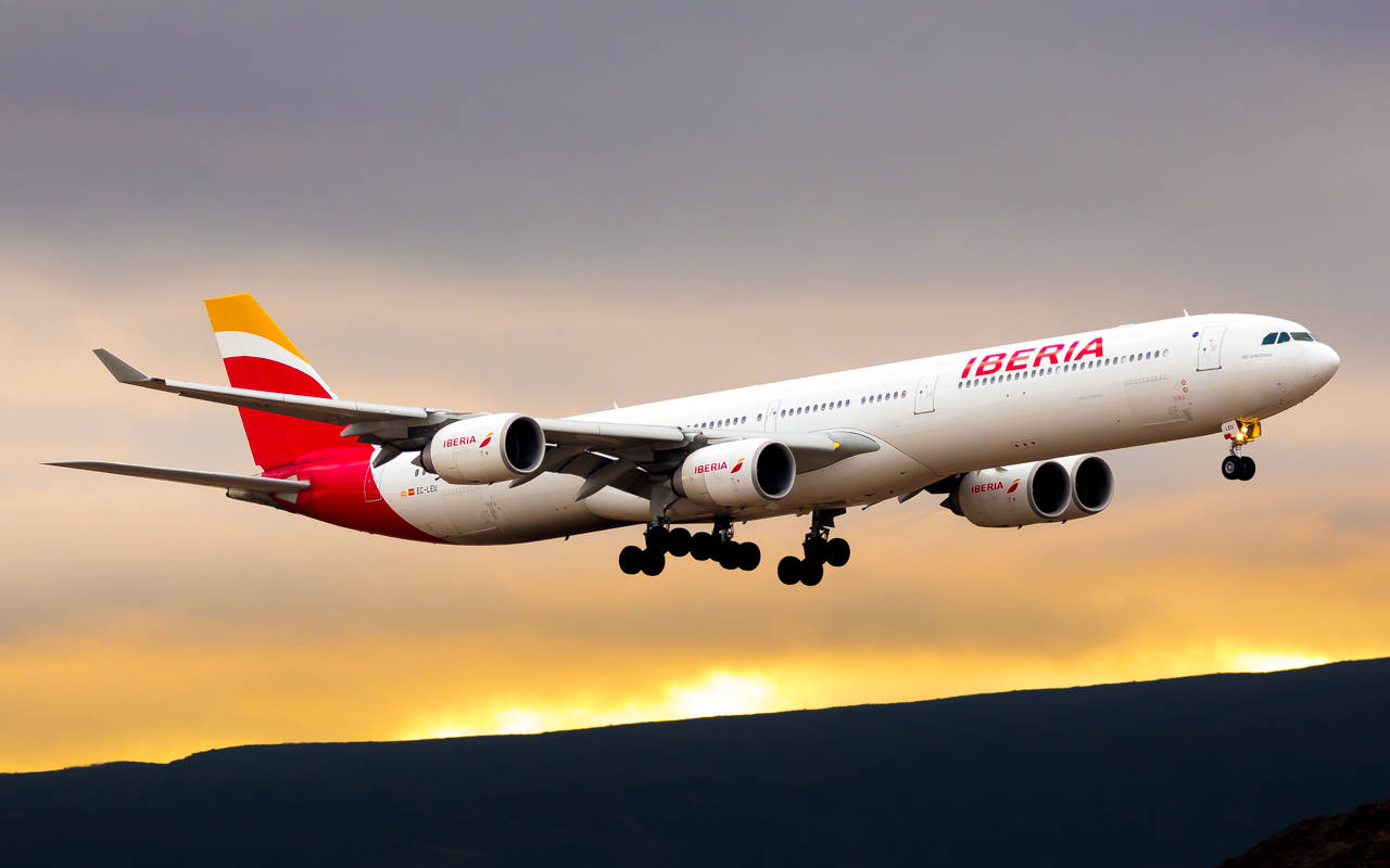 Airport 桌布 壁紙 — 一架伊比利亞航空空巴A340飛機在黑暗山丘上空，對著金色夕陽天空下降，起落架已放下。