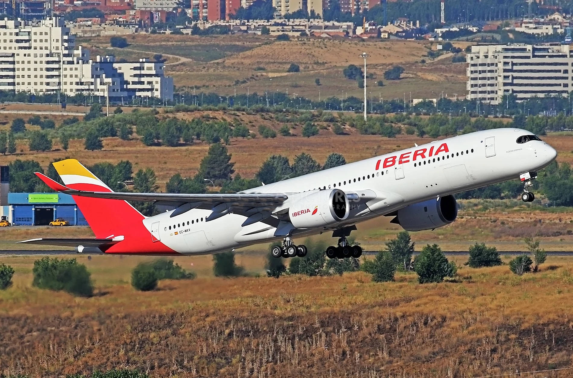  壁紙 — 一架伊比利亞航空空巴A350在都市建築物和乾燥草地背景中優雅降落。