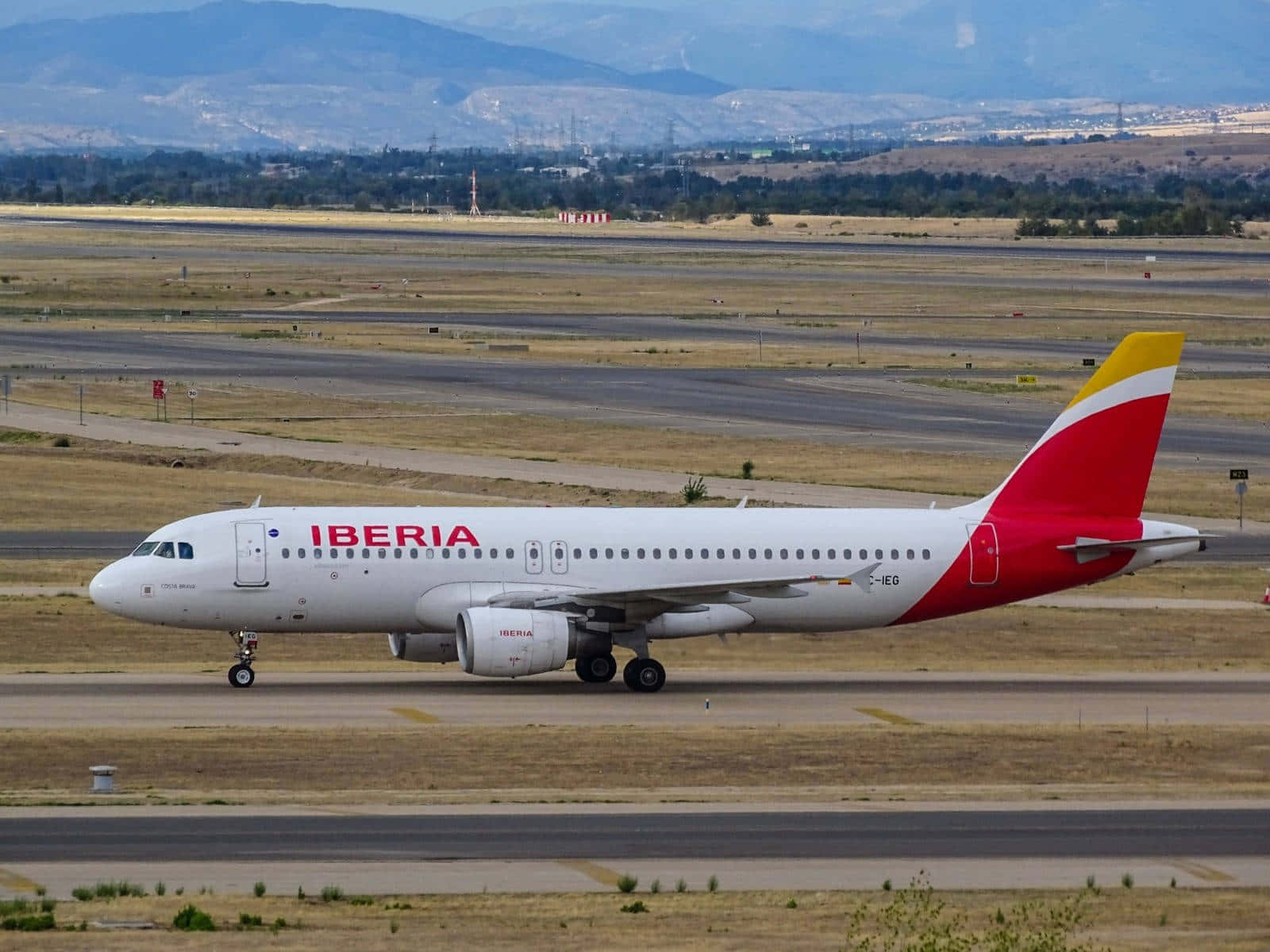 Runway 桌布 壁紙 — 一架伊比利亞航空飛機在晴朗天空下滑行，背景是山脈和乾燥田野。
