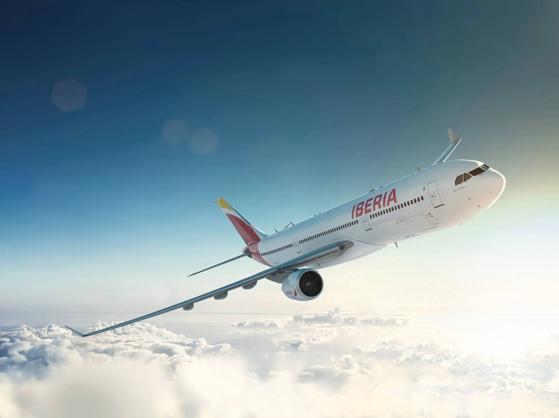 flying 桌布 壁紙 — 一架伊比利亞航空飛機在晴朗藍天和柔和陽光下優雅地翱翔於蓬鬆白雲之上。