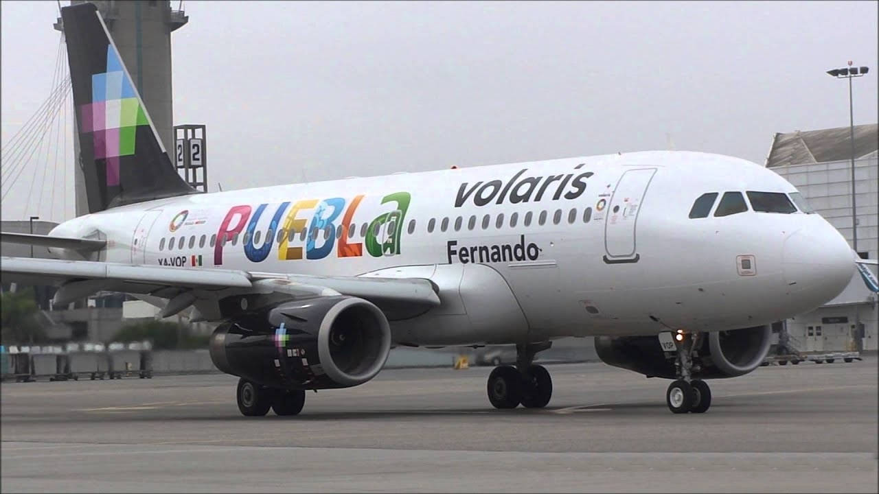 transportation 桌布 壁紙 — 一架側面塗有「PUEBLA」和「Fernando」字樣的Volaris飛機在陰天下的灰色機場停機坪上滑行。