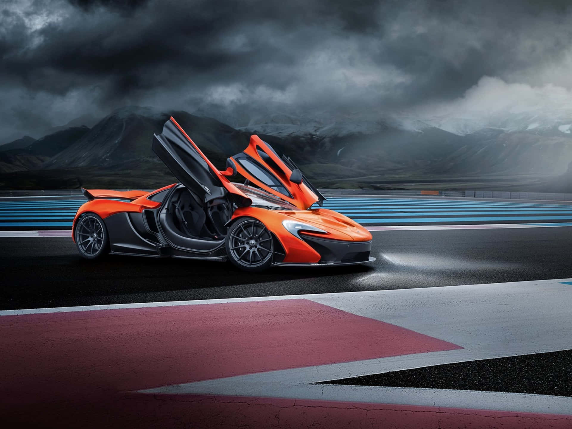 麥拉倫 桌布 壁紙 — 一架充滿活力的橙色McLaren跑車，在暴風雨天空下、背景有積雪山脈的賽道上，打開鷗翼車門。